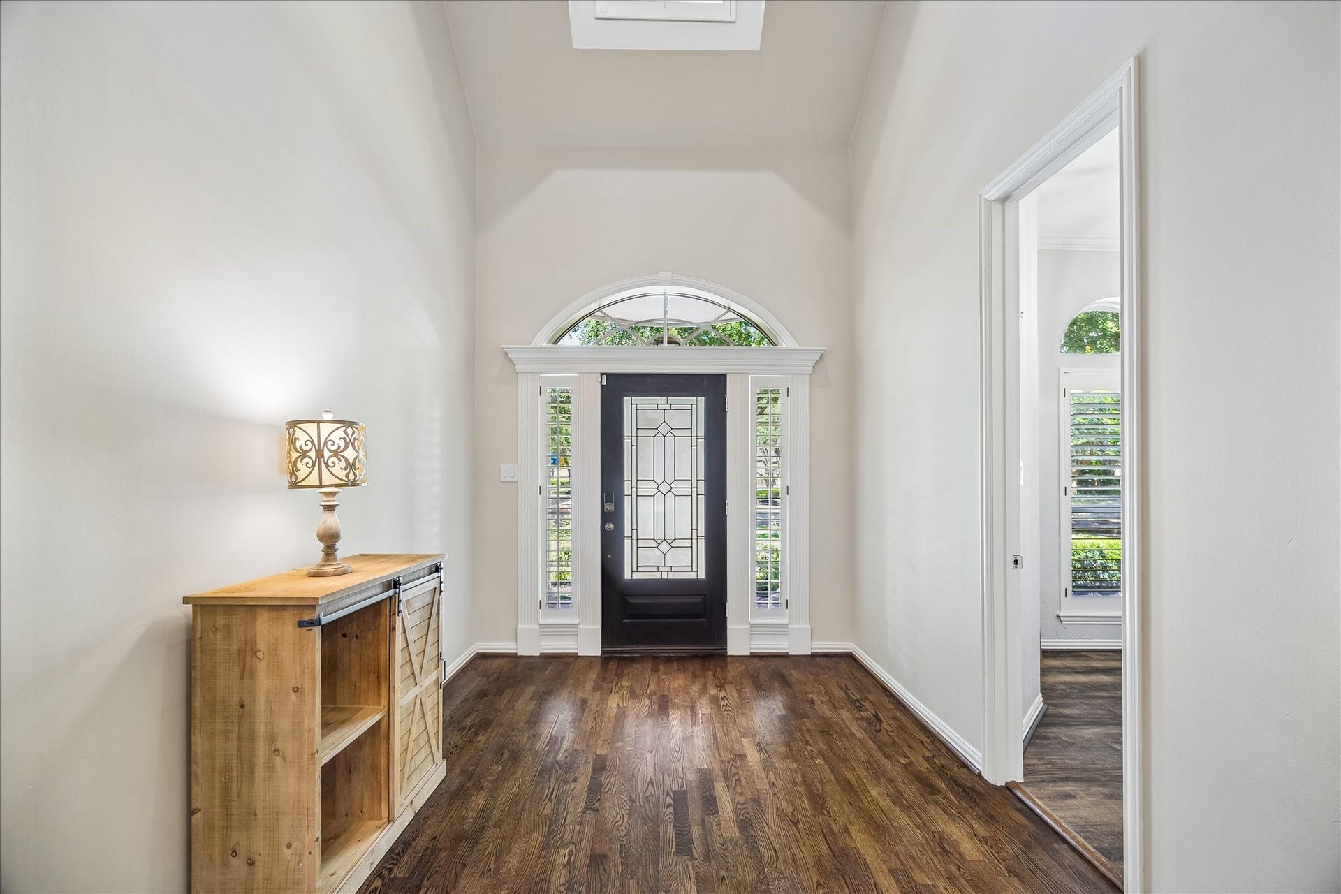 This photo showcases a bright, welcoming entryway with high ceilings, a stylish dark front door featuring decorative glass, and rich hardwood floors.