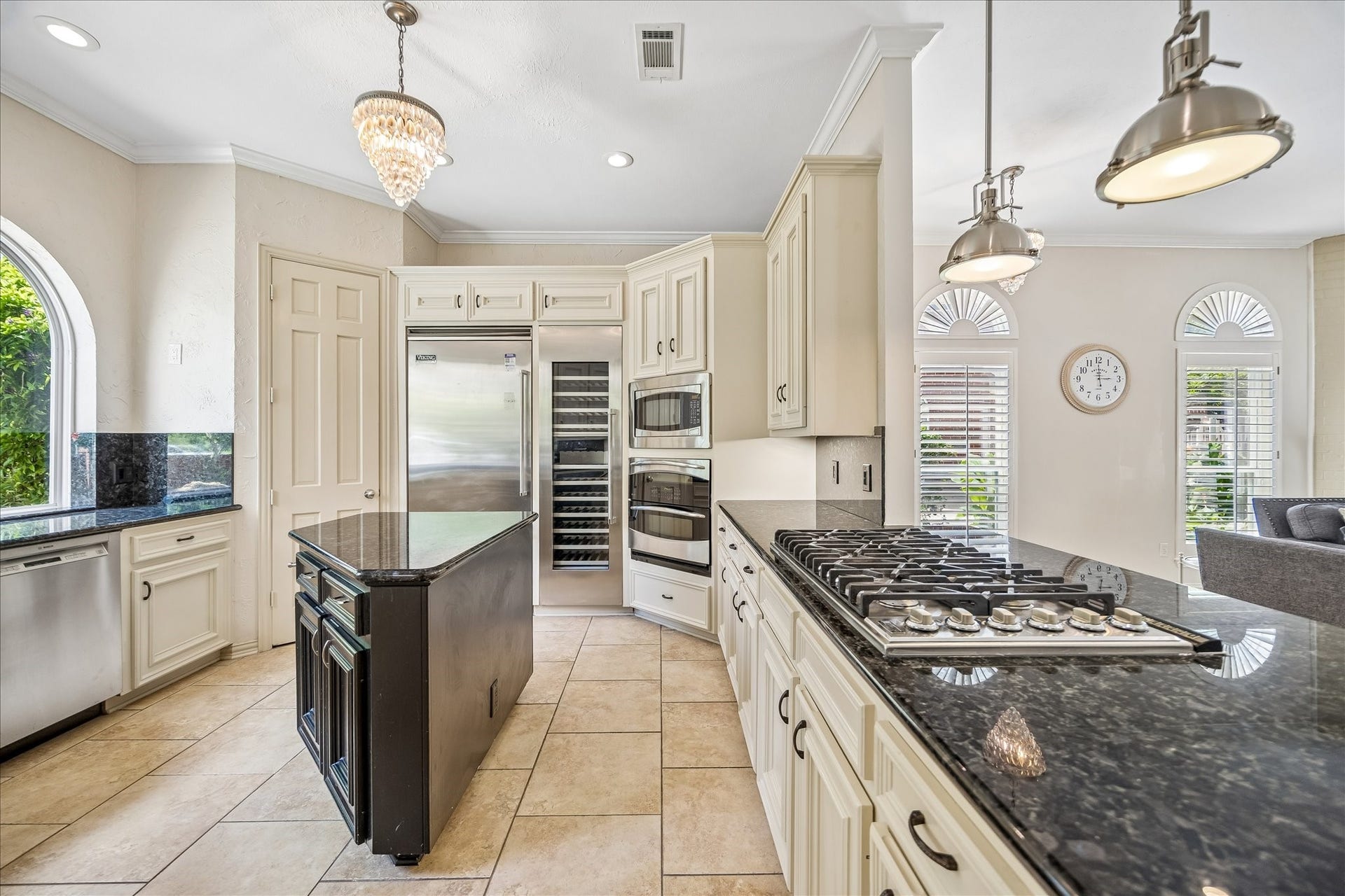 This kitchen features modern stainless steel appliances, including a Viking refrigerator, double oven, warming drawer, beverage refrigerator, and a large wine cooler. Kitchen includes granite countertops, a central island, and ample cabinetry. Large windows provide natural light, and elegant light fixtures add sophistication.