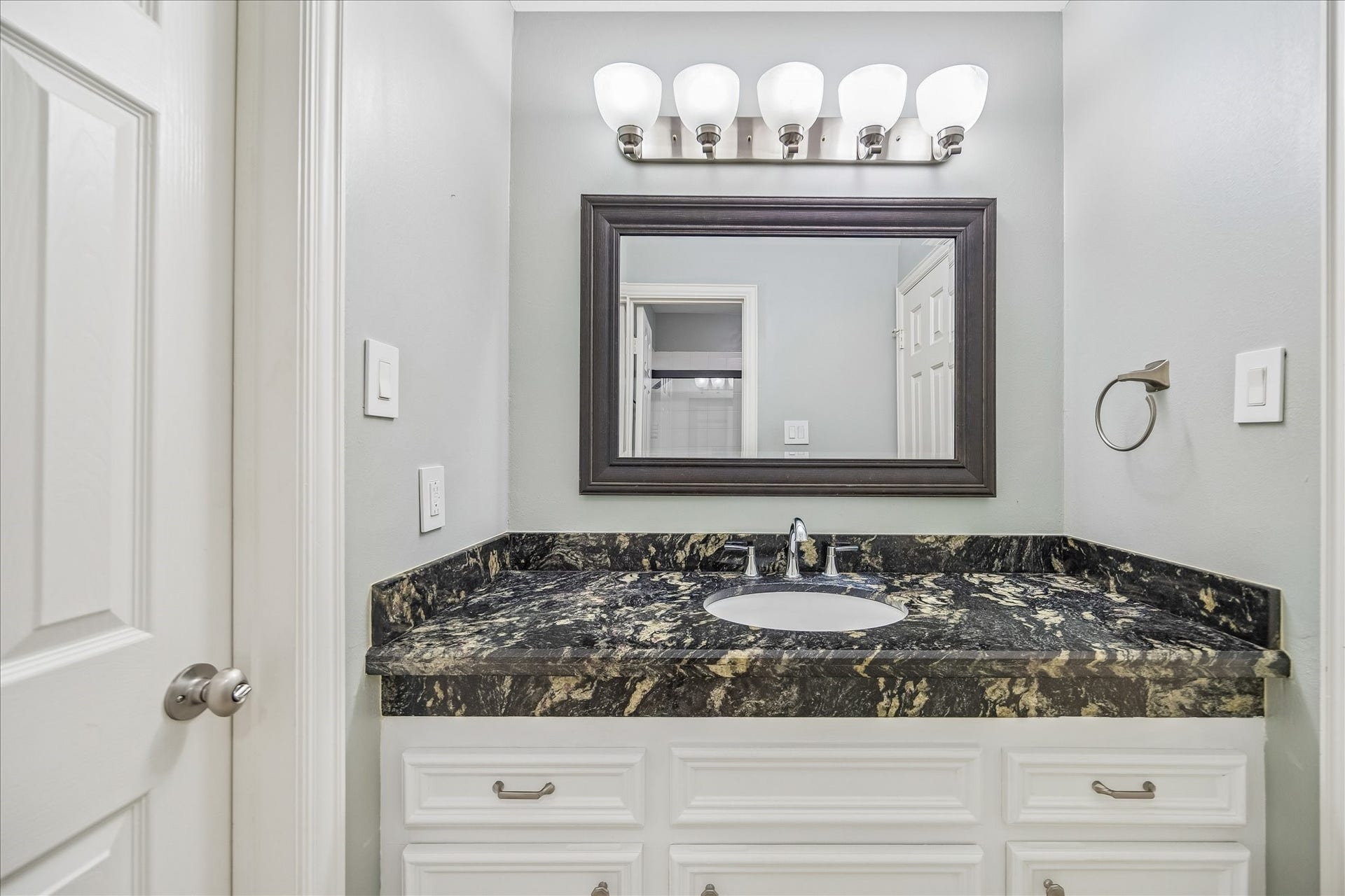 The other upstairs bathroom features a stylish vanity with a gorgeous countertop, undermount sink, and modern designer faucet. A large framed mirror and sleek overhead lighting provide ample illumination, while crisp white cabinetry, with elegant hardware, completes the space.