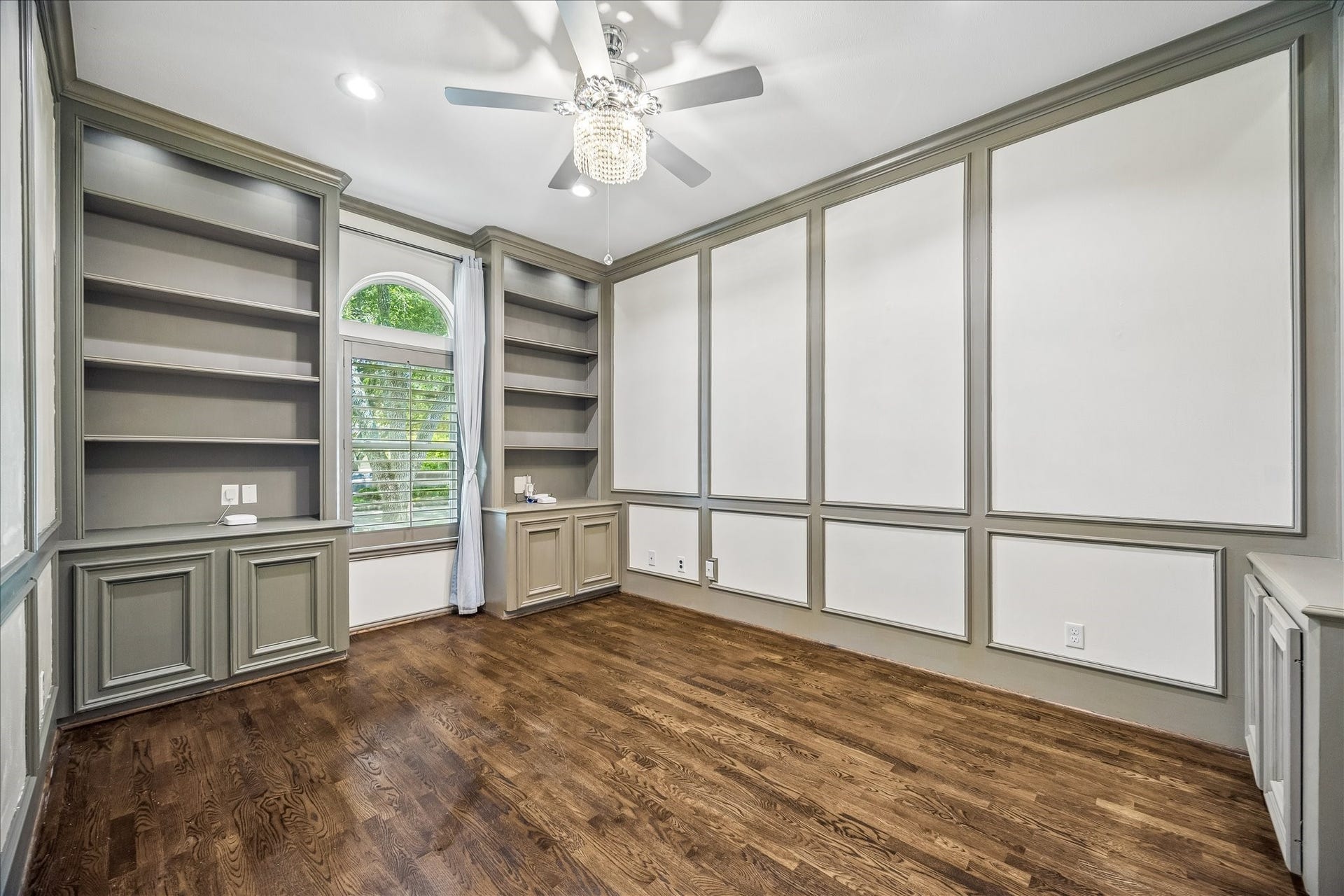 This exquisite home office, conveniently located near the primary suite, has  built-in shelving, paneling, and cabinetry, along with a large window.