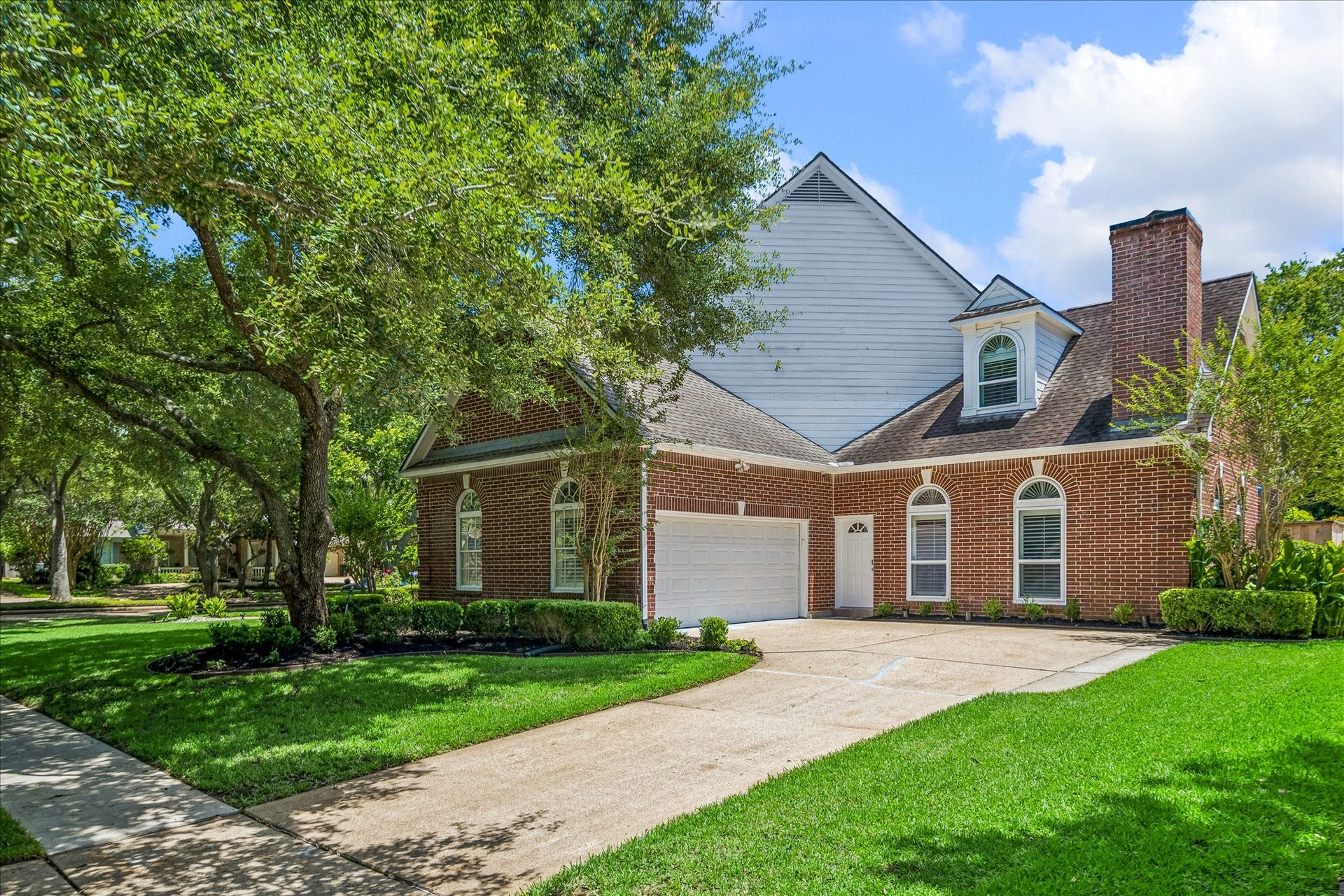 This inviting brick home features a two-car garage with epoxy floor, arched windows, and a charming dormer. The well-maintained yard with lush greenery and mature trees offers excellent curb appeal, set on a quiet, tree-lined street.
