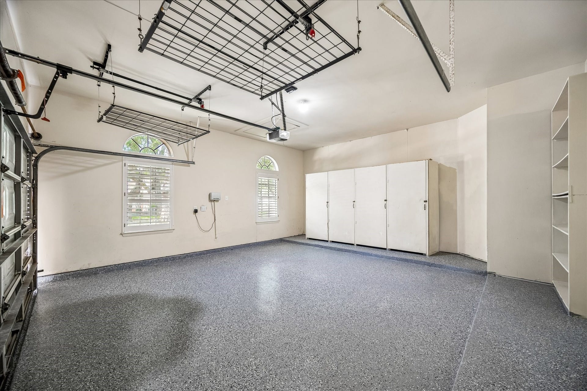 What a garage! Featuring a newly installed epoxy floor (May 2026), this impressive space is both functional and refined. It offers built-in storage cabinets and overhead racks for exceptional organization, along with two large windows dressed with shutters that provide abundant natural light.