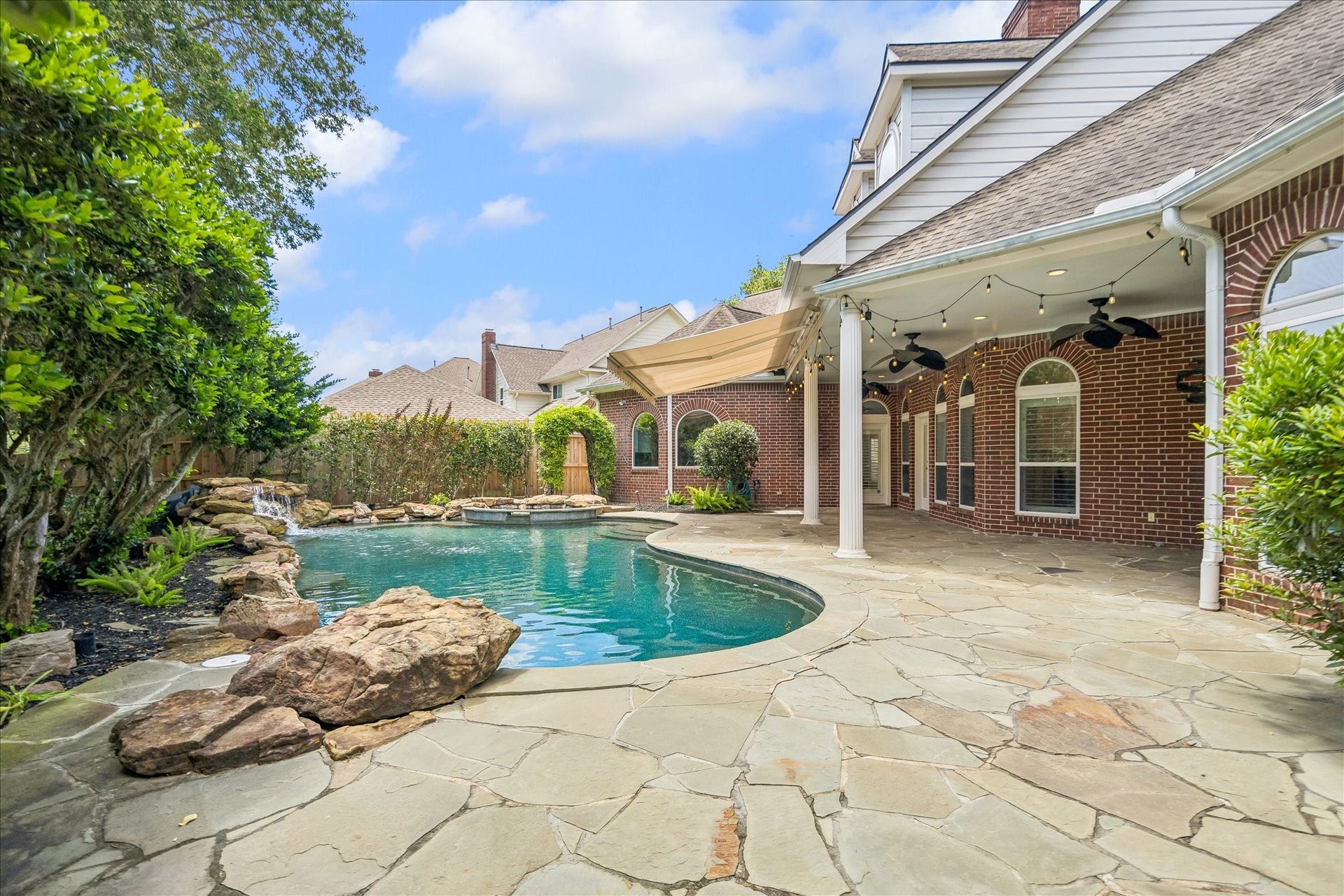 Beautifully landscaped pool, surrounded by flagstone and lush greenery, creates a serene outdoor retreat. 
The homes classic red brick exterior adds timeless charm and enhances the overall warm, inviting aesthetics.