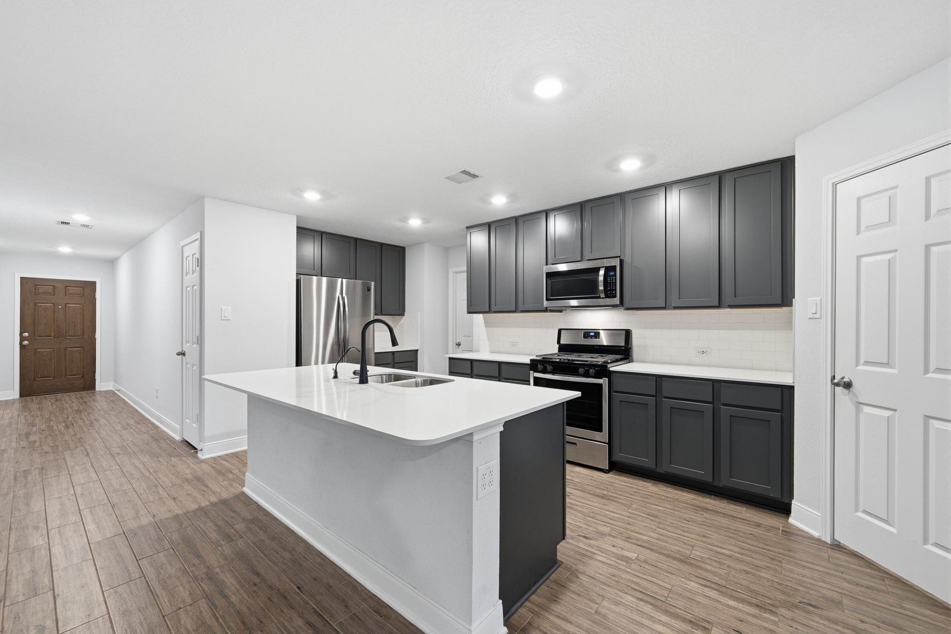 10314 Russell Pines Drive, Rosharon, TX 77583 Modern kitchen with sleek gray cabinetry, stainless steel appliances, and a spacious island, complemented by sleek flooring and bright recessed lighting.