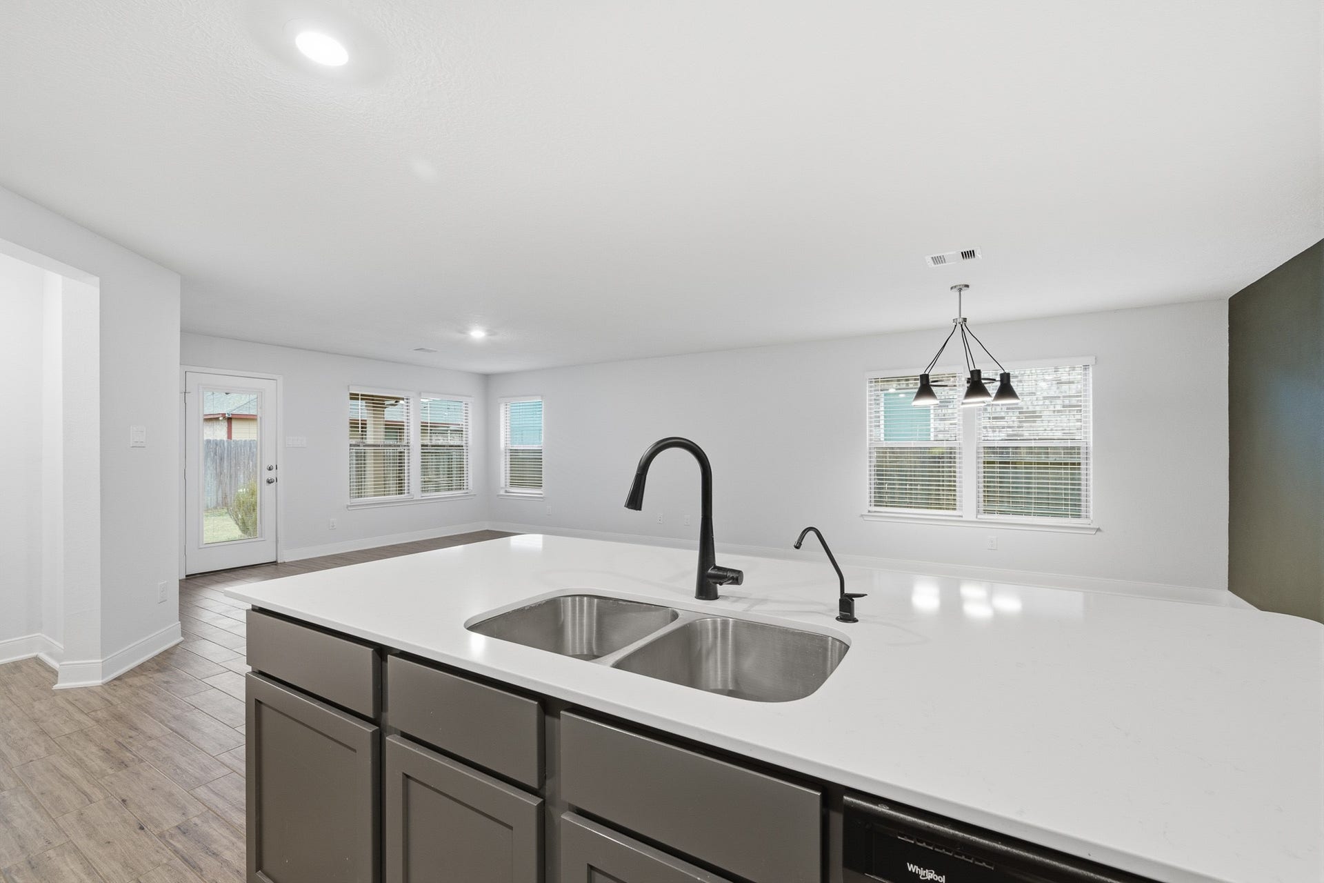 10314 Russell Pines Drive, Rosharon, TX 77583 Spacious open-plan kitchen and living area featuring a sleek island with a modern sink, stylish light fixtures, and abundant natural light from large windows and a patio door.