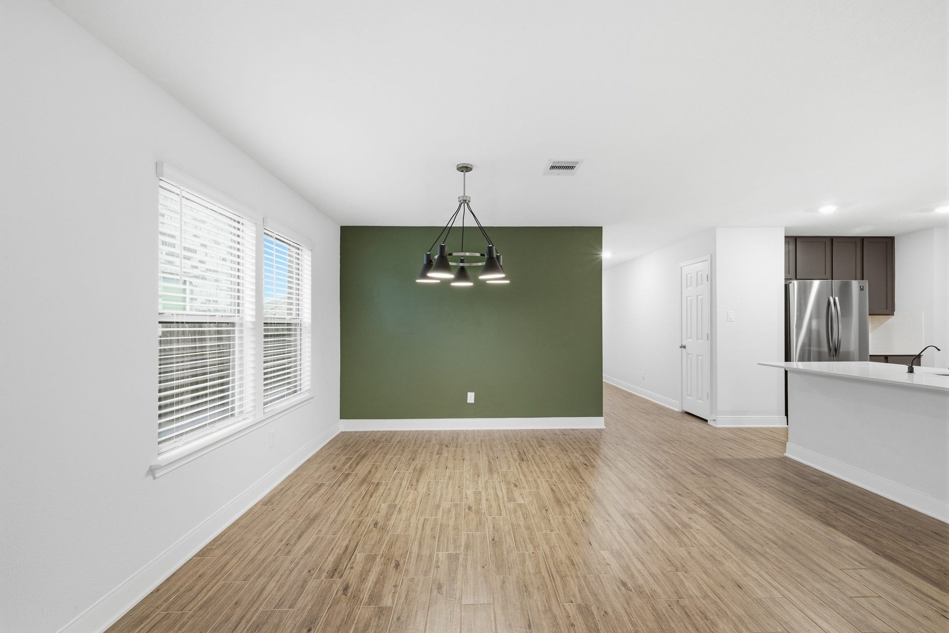10314 Russell Pines Drive, Rosharon, TX 77583 Bright and inviting dining area with sleek flooring, accented by a stylish green feature wall and modern light fixture, adjacent to an open-concept kitchen.