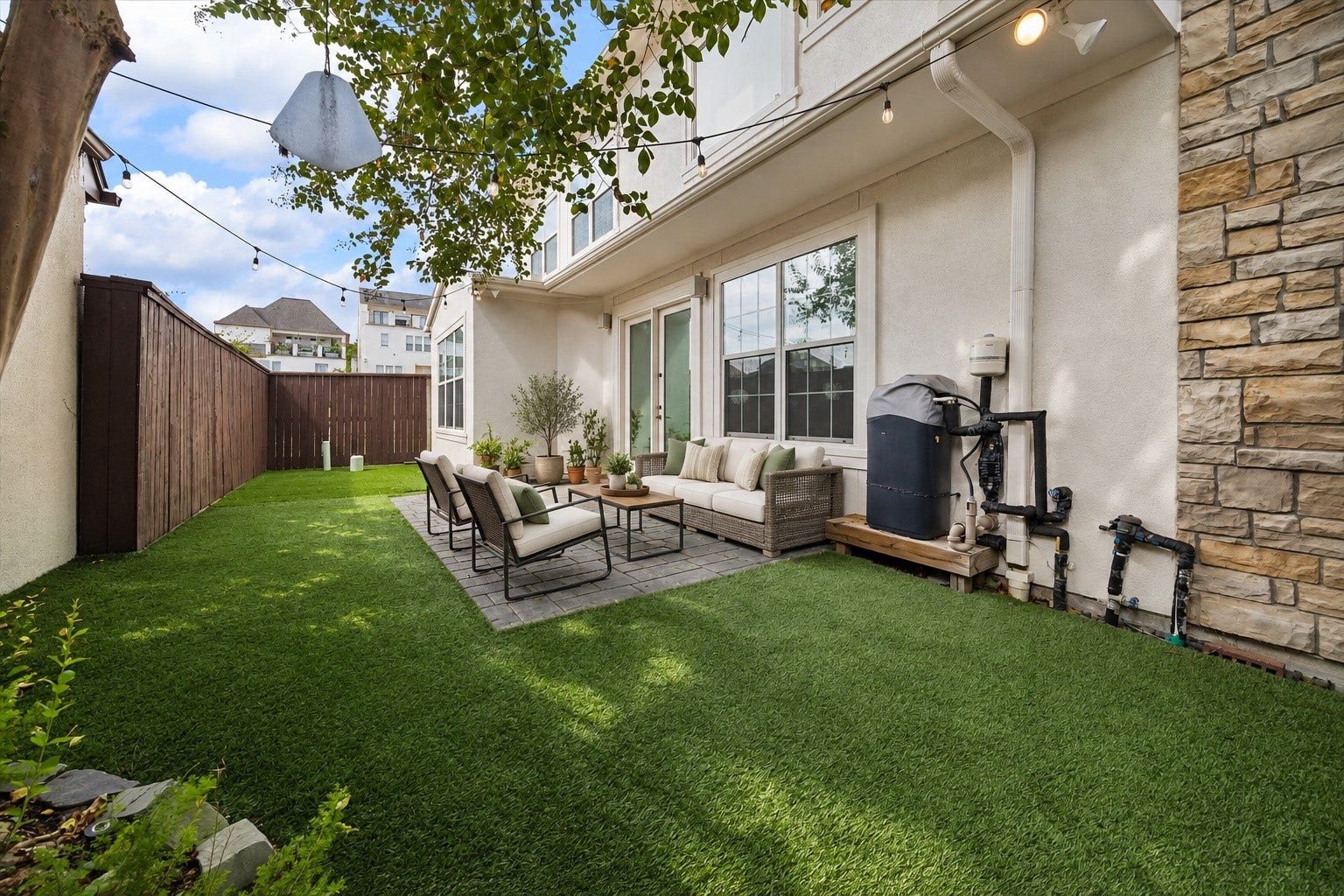 1311 N Jordan Cove, Houston, TX 77055 Another perspective of the inviting backyard showcasing the combination of paved patio & turfed green space. String lights, outdoor speakers & floodlights create a wonderful setting for outdoor gatherings, morning coffee or relaxing at the end of the day. Half of the turf was replaced in 2026! (Photo virtually enhanced/furnishings virtually staged).