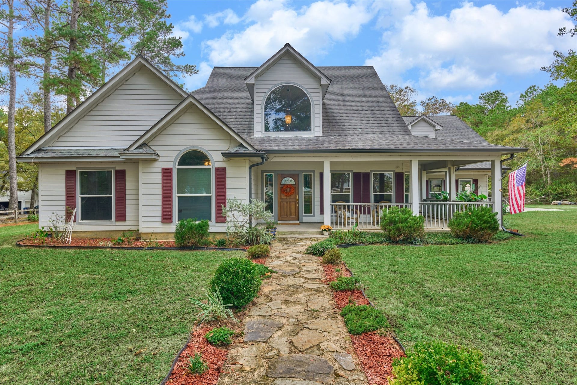 28911 Sapphire Circle, Magnolia, TX 77355 Beautiful two-story custom home with inviting front porch, manicured landscaping, and a welcoming stone pathway, nestled among mature trees.