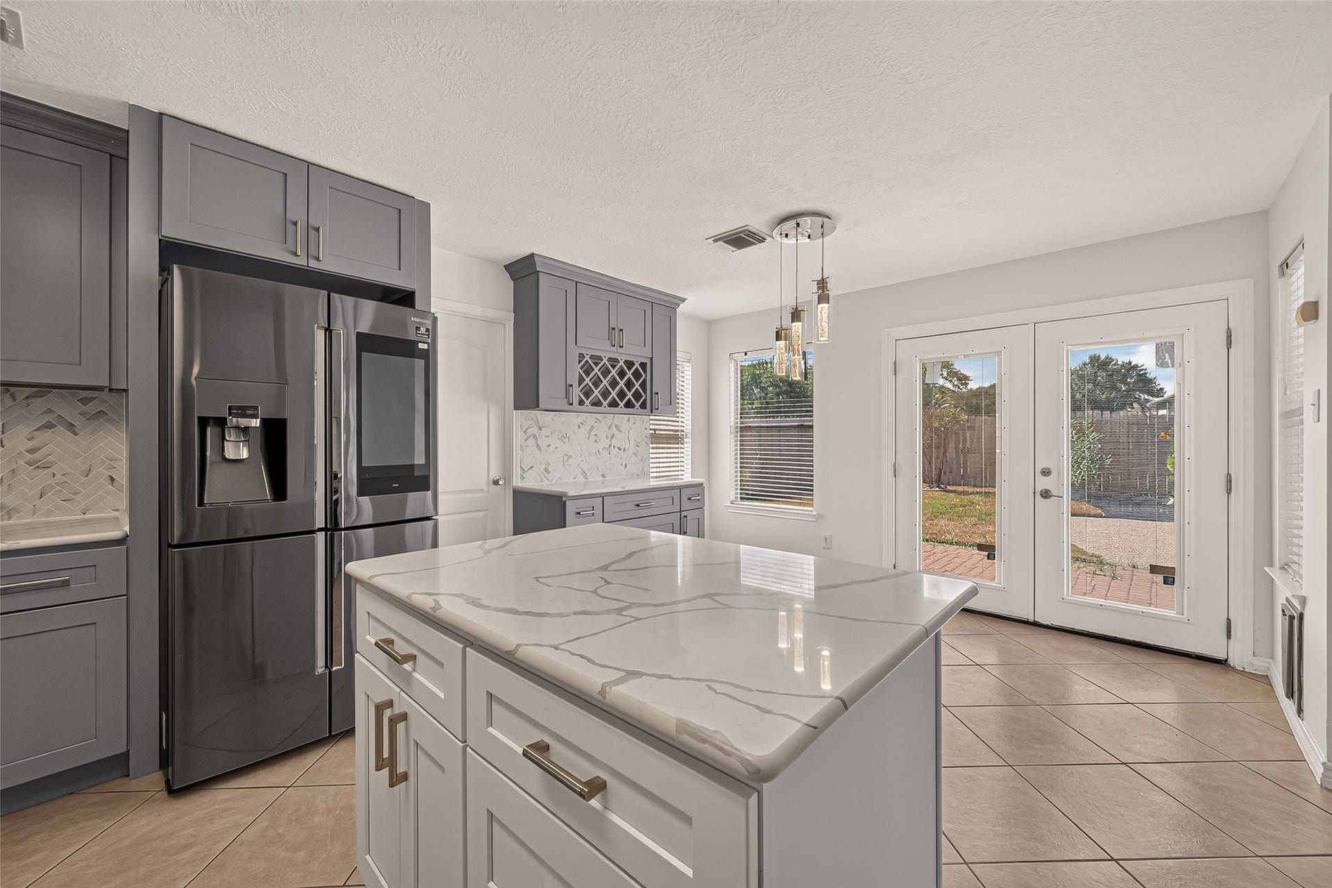 3111 Lantern Bay Lane, Katy, TX 77449 The kitchen island takes center stage in this view, with sweeping quartz countertops, ample prep space, a stainless steel refrigerator, and French doors leading to the backyard.
