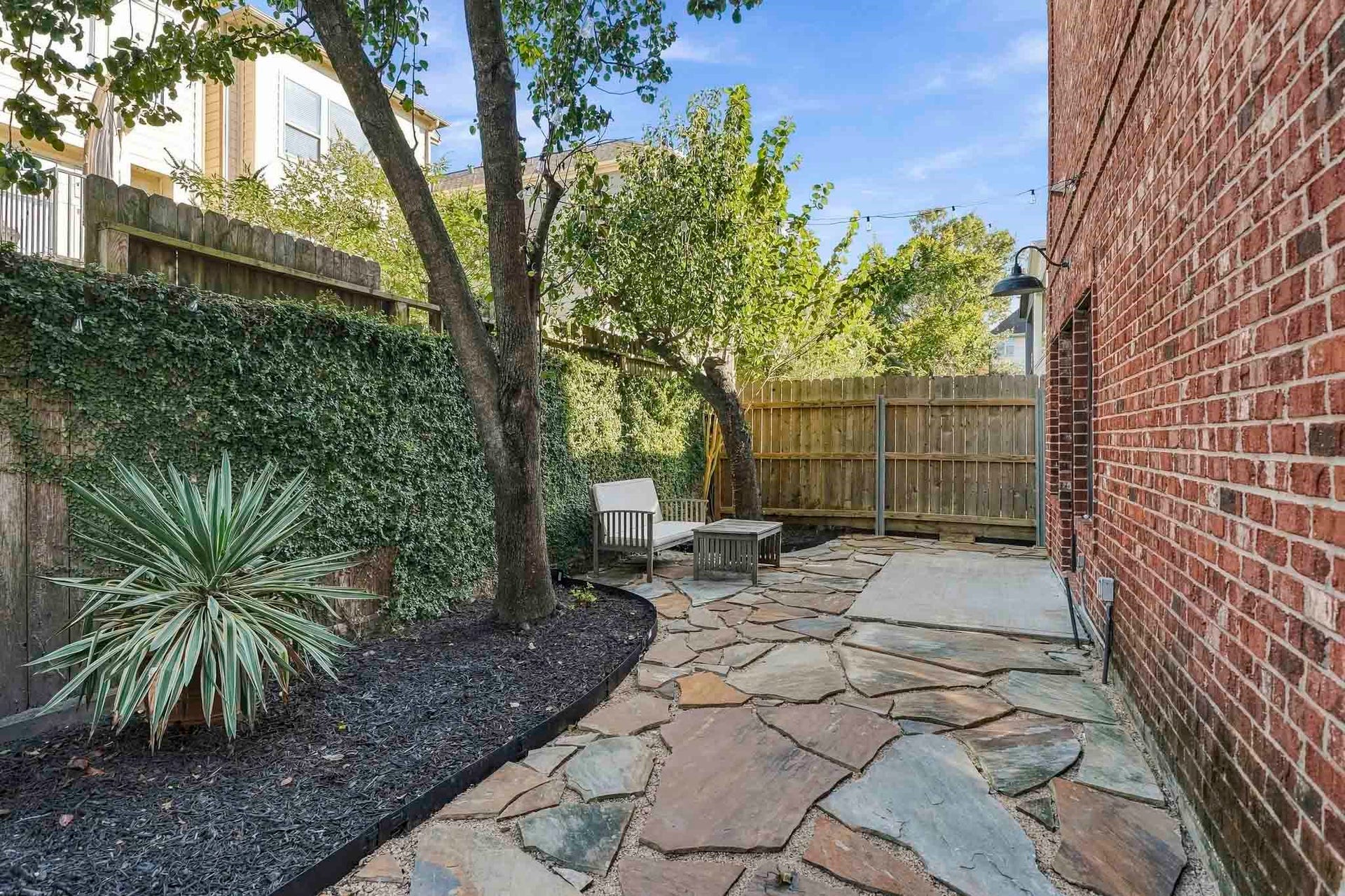 910 Malone Street, #106, Houston, TX 77007 Mature shade trees and the patio adorned with string lights creates a charming outdoor ambiance, offering a beautiful setting for relaxing beneath the canopy or enjoying evenings under the stars.