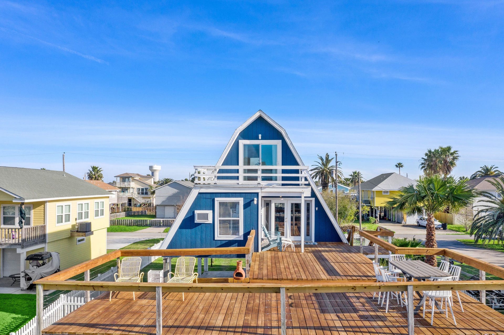 16610 Nassau Way, Galveston, TX 77554 Charming A-frame home with a spacious wooden deck perfect for outdoor entertaining, surrounded by palm trees in a serene neighborhood setting.