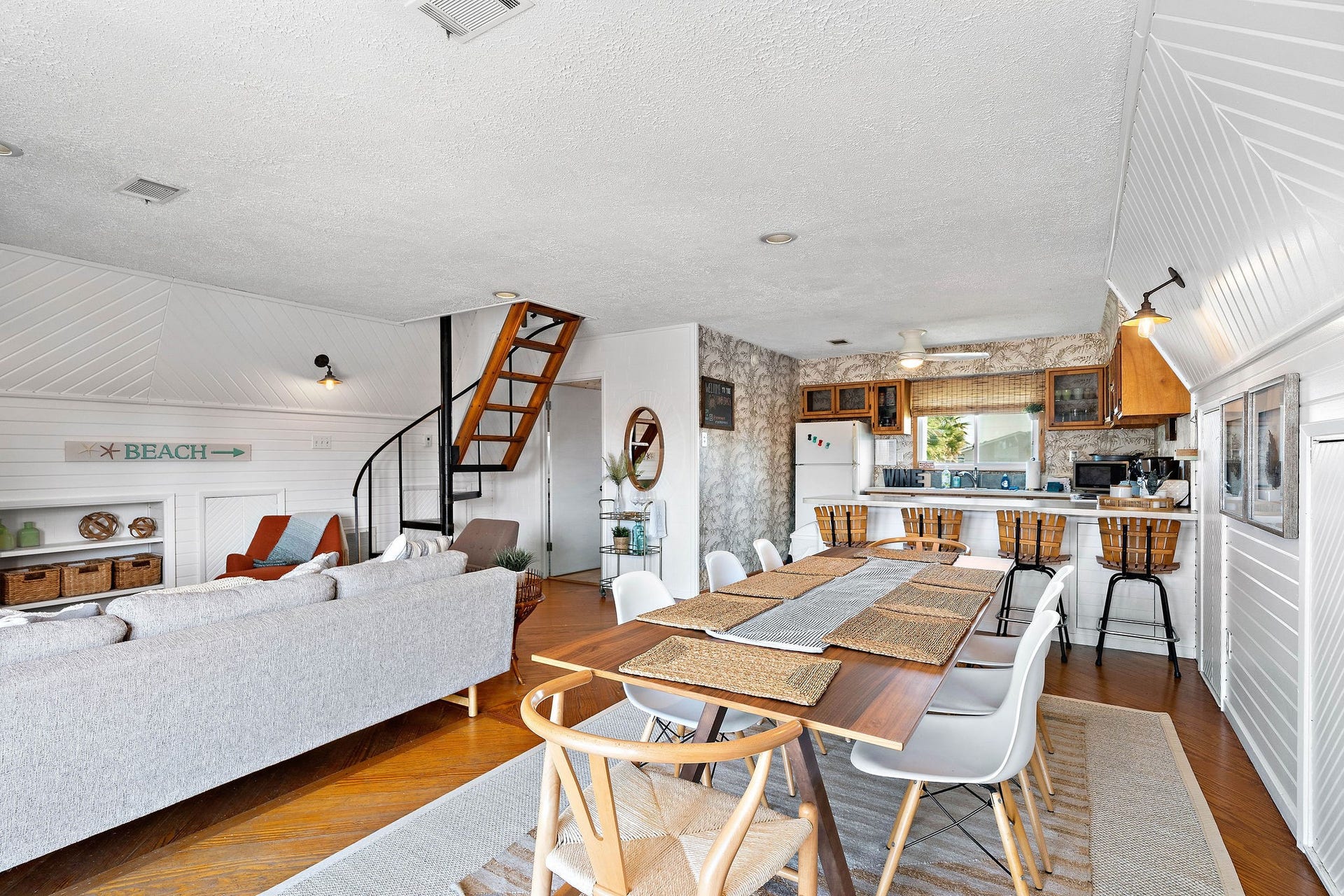 16610 Nassau Way, Galveston, TX 77554 Charming open-concept living space with a cozy seating area, stylish dining table, and a kitchen featuring rustic wood accents. The spiral staircase adds character, and the beach-themed dcor creates a relaxed, inviting atmosphere.