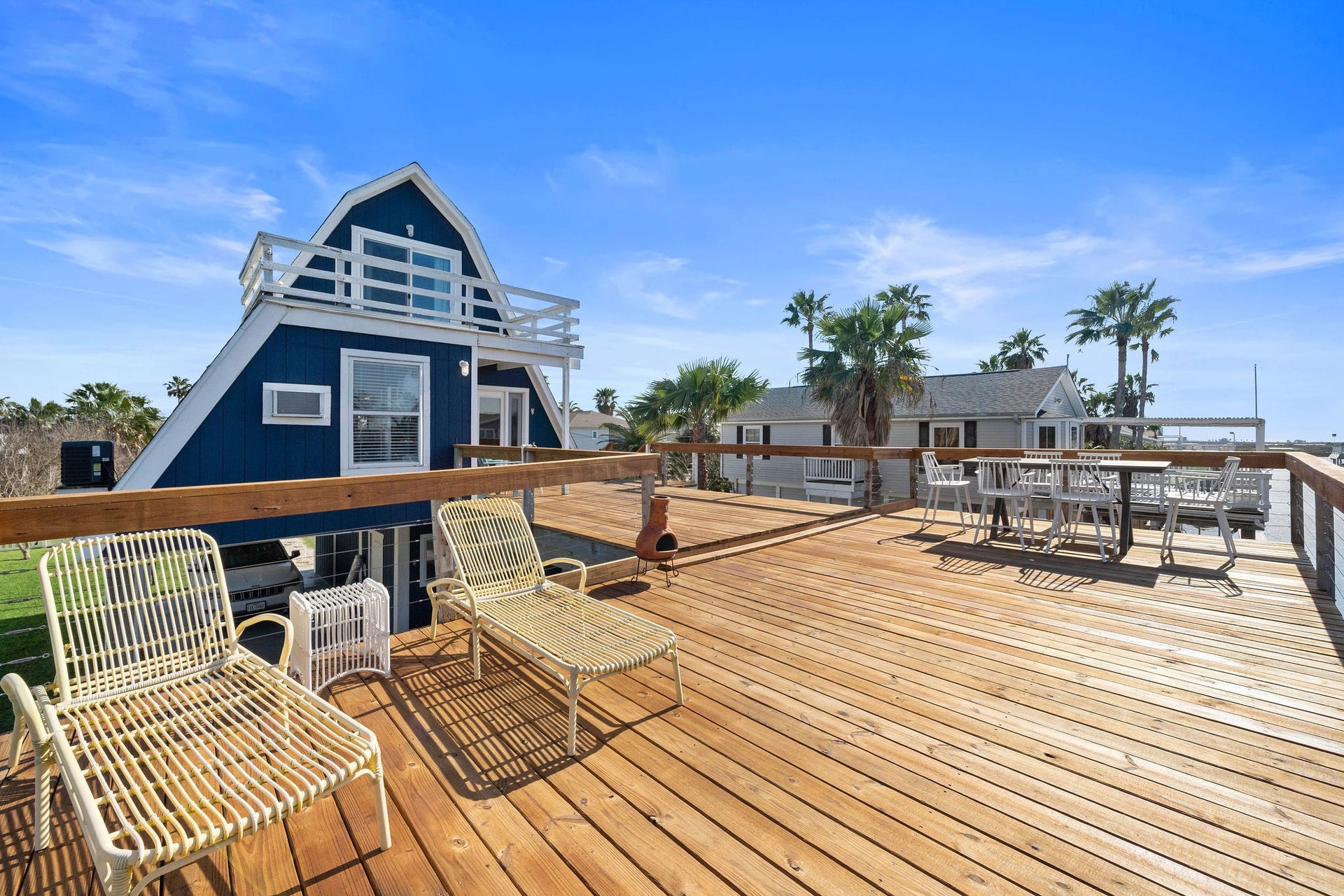 16610 Nassau Way, Galveston, TX 77554 Charming A-frame home with a spacious wooden deck, perfect for outdoor relaxation and entertaining, surrounded by lush palm trees.