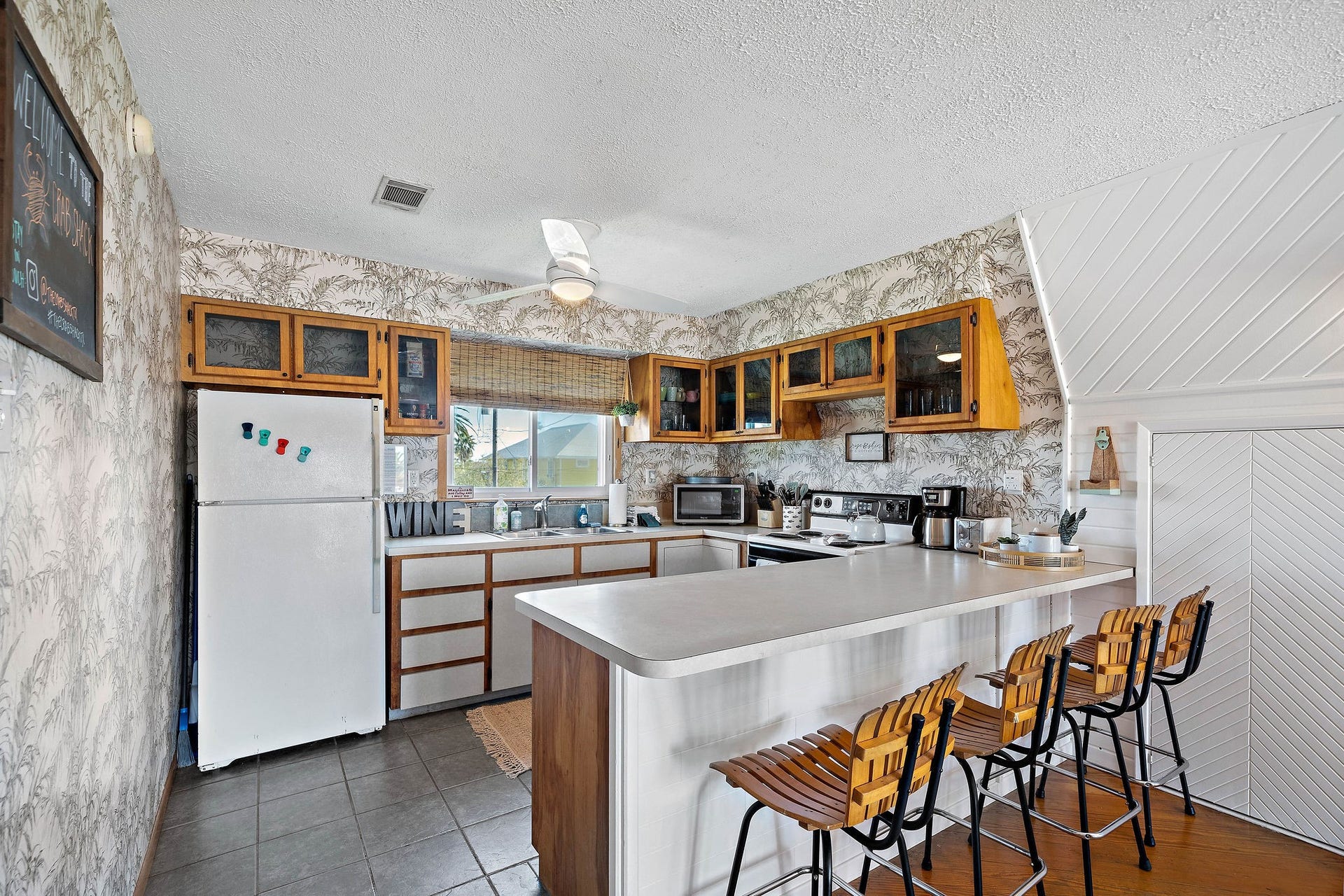 16610 Nassau Way, Galveston, TX 77554 Charming kitchen with rustic wooden cabinetry, a spacious breakfast bar with seating, and modern appliances set against a stylish patterned wallpaper.