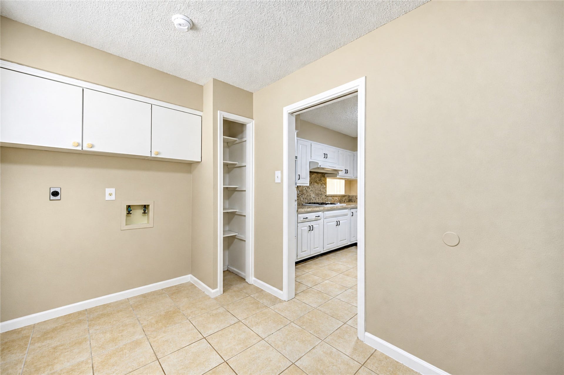 361 Champions Colony III, Houston, TX 77069 Spacious utility room with tile flooring, built-in cabinets, and a convenient open doorway leading to a modern kitchen with white cabinetry and a granite backsplash.