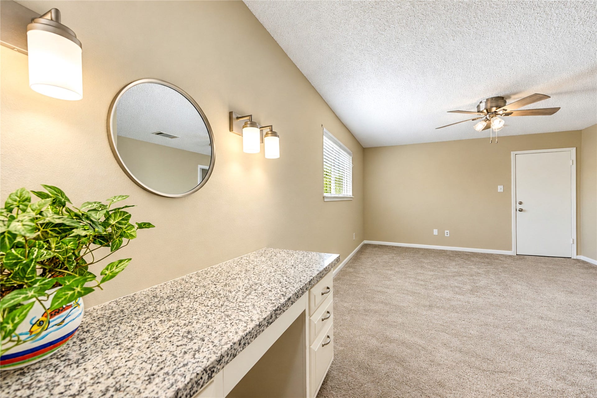 361 Champions Colony III, Houston, TX 77069 Spacious master bedroom with neutral tones, featuring plush carpeting, a brand new ceiling fan, and abundant natural light. A stylish vanity with a granite countertop and modern lighting adds elegance.