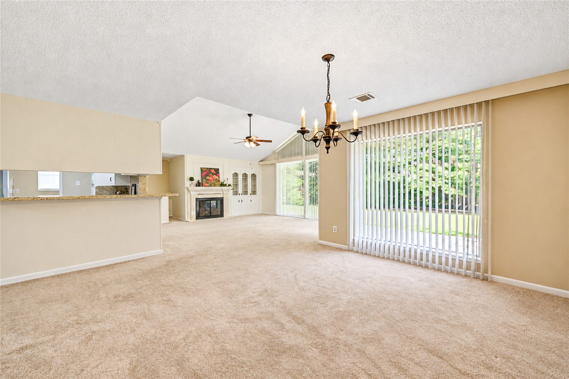 361 Champions Colony III, Houston, TX 77069 Spacious living area with an open layout, featuring a cozy fireplace, large windows with vertical blinds offering abundant natural light, and a charming chandelier over the dining space.