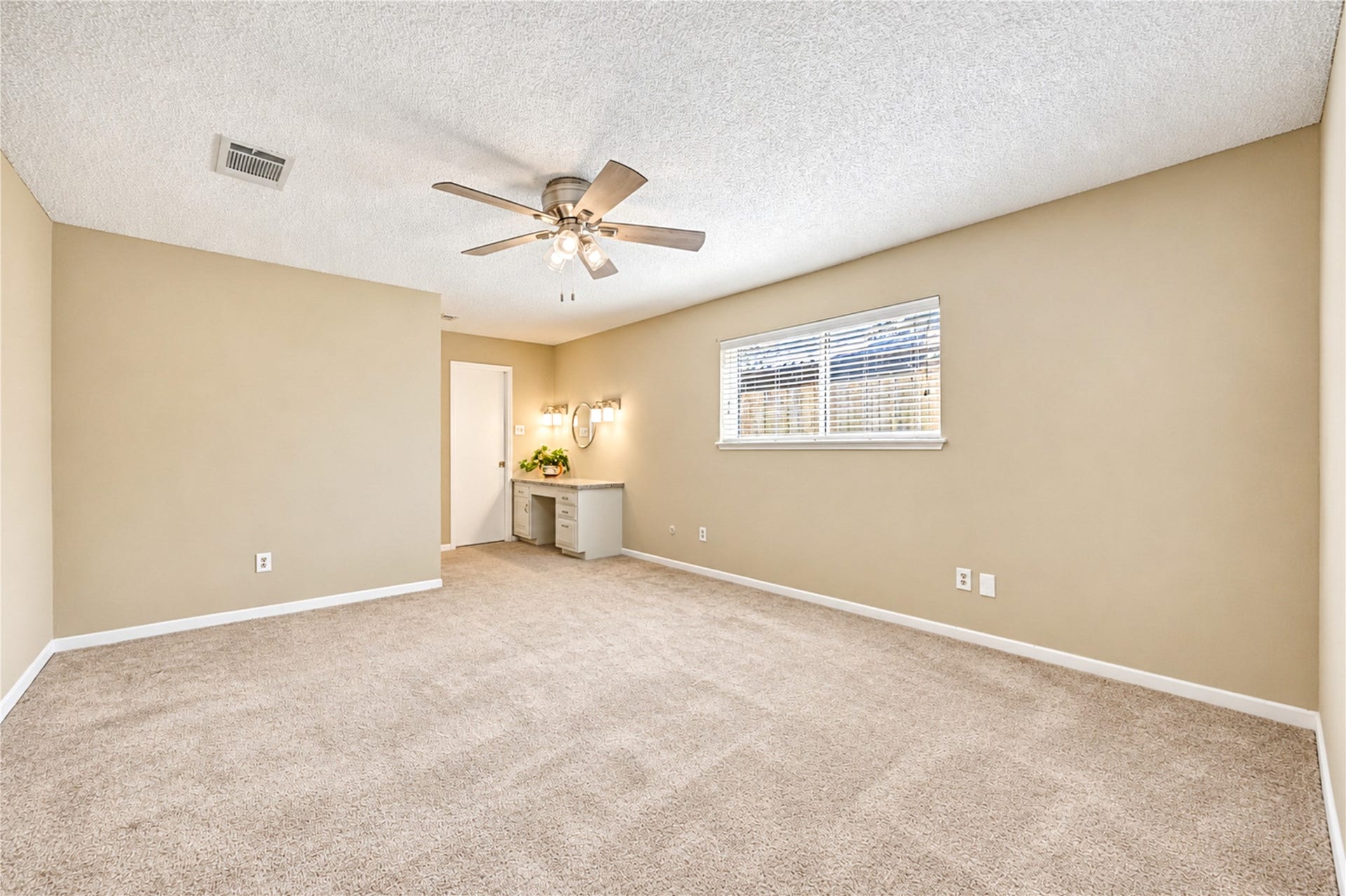 361 Champions Colony III, Houston, TX 77069 Spacious bedroom with plush carpeting and warm neutral walls, featuring a ceiling fan and a cozy vanity area with natural light from a large window.