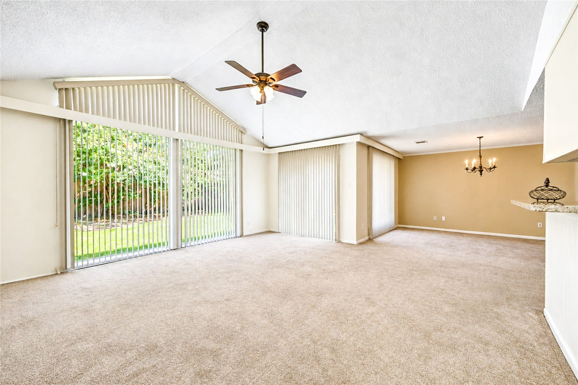 361 Champions Colony III, Houston, TX 77069 Spacious living area with vaulted ceilings and abundant natural light streaming through large windows, complemented by a stylish ceiling fan and elegant chandelier.
