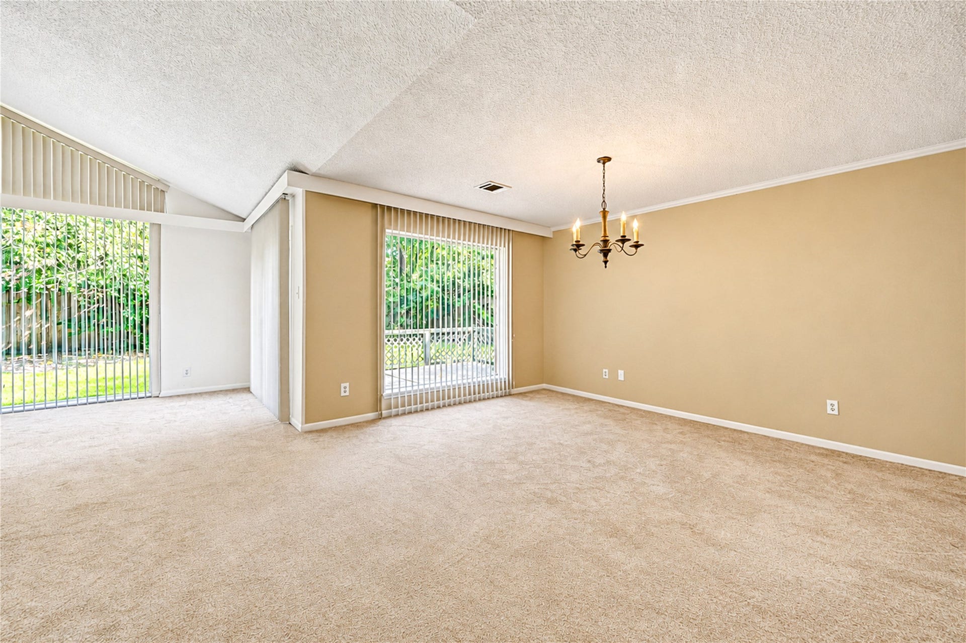 361 Champions Colony III, Houston, TX 77069 Spacious living area with plush carpeting, a stylish chandelier, and large windows offering abundant natural light and garden views.