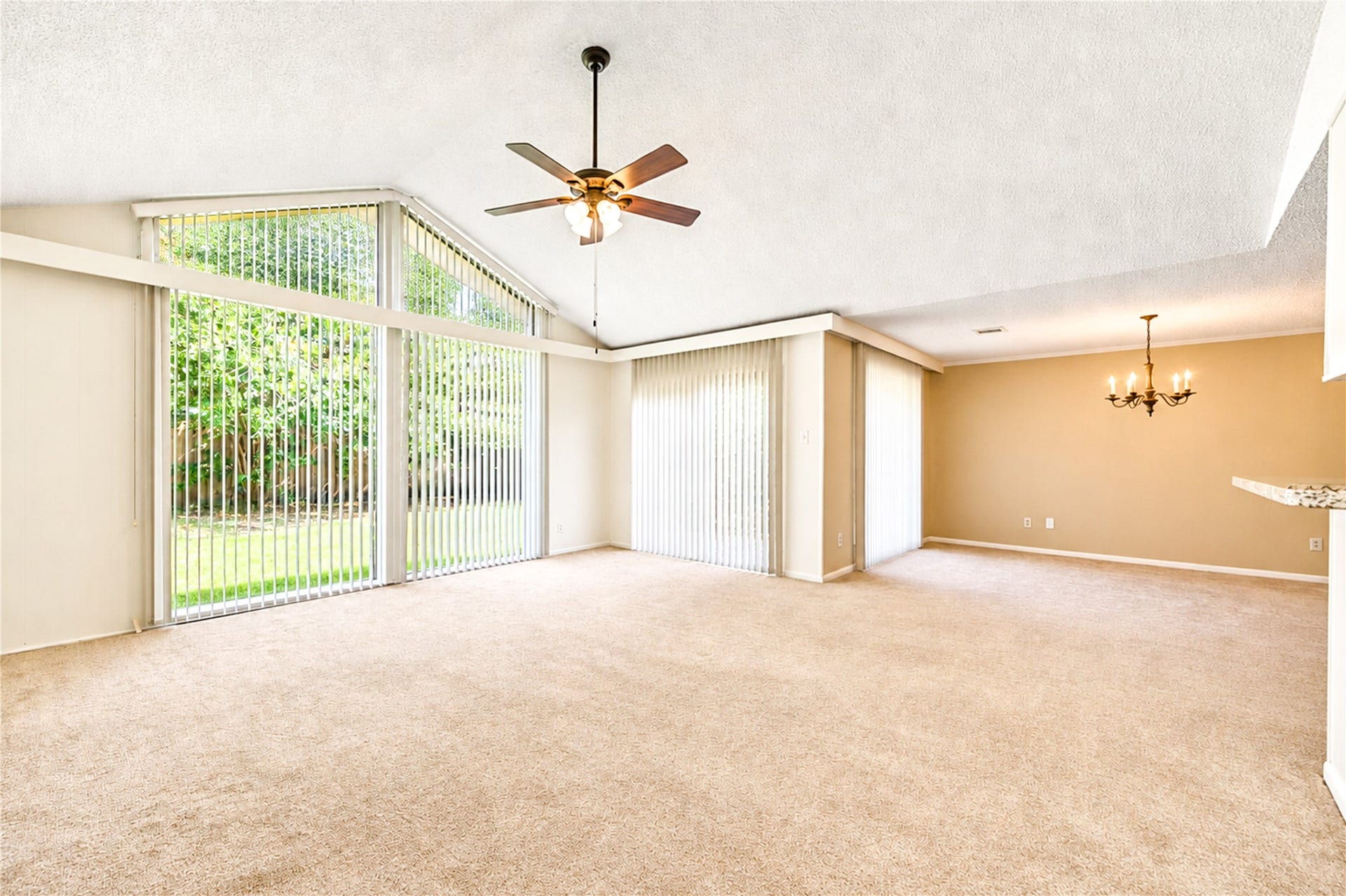 361 Champions Colony III, Houston, TX 77069 Spacious living area with vaulted ceilings and abundant natural light from large windows, complemented by a cozy carpeted floor and elegant chandelier.