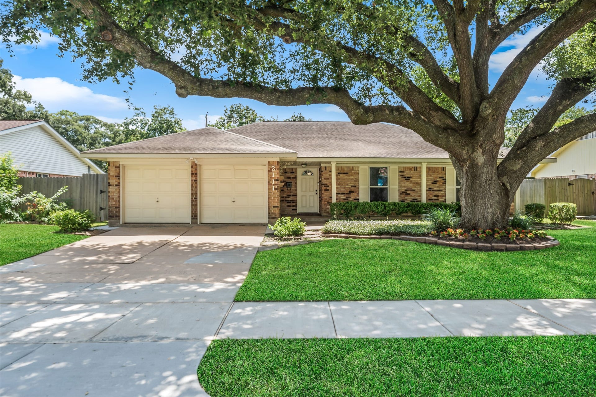 2111 Willow Boulevard, Pearland, TX 77581 This charming home features a classic brick exterior with a welcoming front porch. It includes a two-car garage and a beautifully landscaped front yard, highlighted by a large, mature tree offering ample shade.