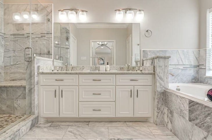 1013 10th Street, Galveston, TX 77550 Luxurious primary bathroom featuring elegant marble finishes, a spacious glass-enclosed shower, dual sinks with sleek fixtures, and a relaxing soaking tub.