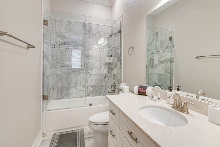1013 10th Street, Galveston, TX 77550 Elegant guest bathroom featuring a sleek glass-enclosed shower, sophisticated marble tile, and a modern vanity for a touch of luxury.
