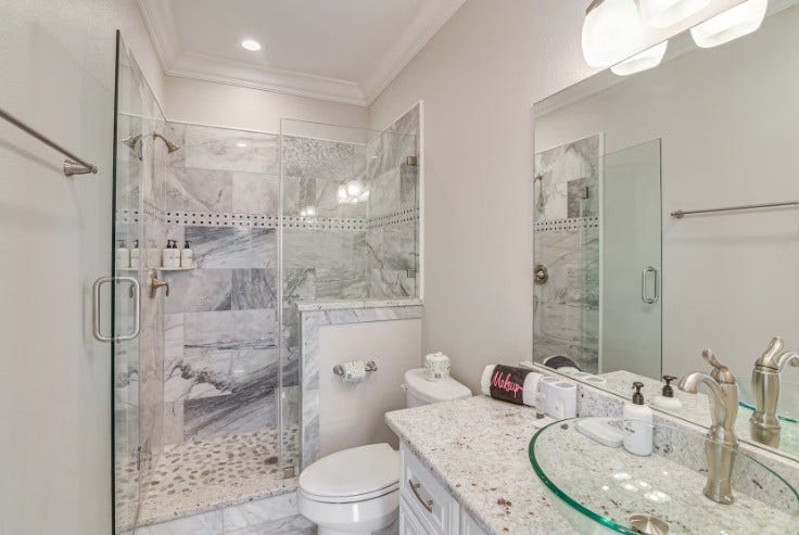1013 10th Street, Galveston, TX 77550 Elegant guest bathroom featuring a sleek glass-enclosed shower, luxurious marble tile, and modern fixtures for a touch of sophistication.