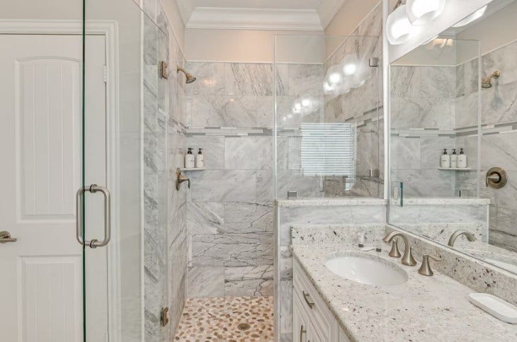 1013 10th Street, Galveston, TX 77550 Luxurious primary bathroom featuring elegant marble finishes, a spacious glass-enclosed shower, and modern fixtures for a spa-like retreat.