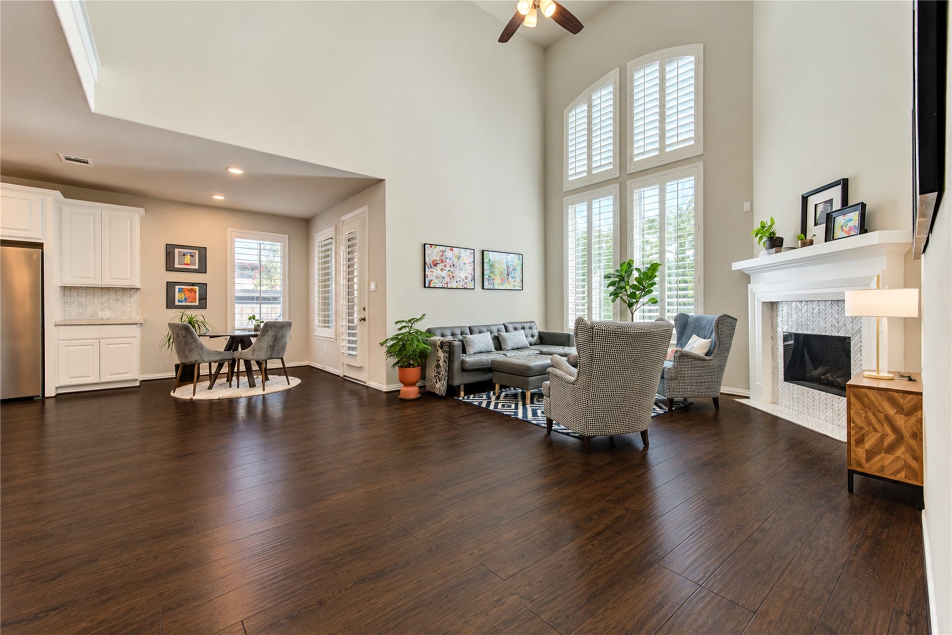 The dramatic double-height ceiling creates a grand, airy feel in the living room, complemented by a tall gas fireplace with a stylish tile surround that serves as a striking focal point.