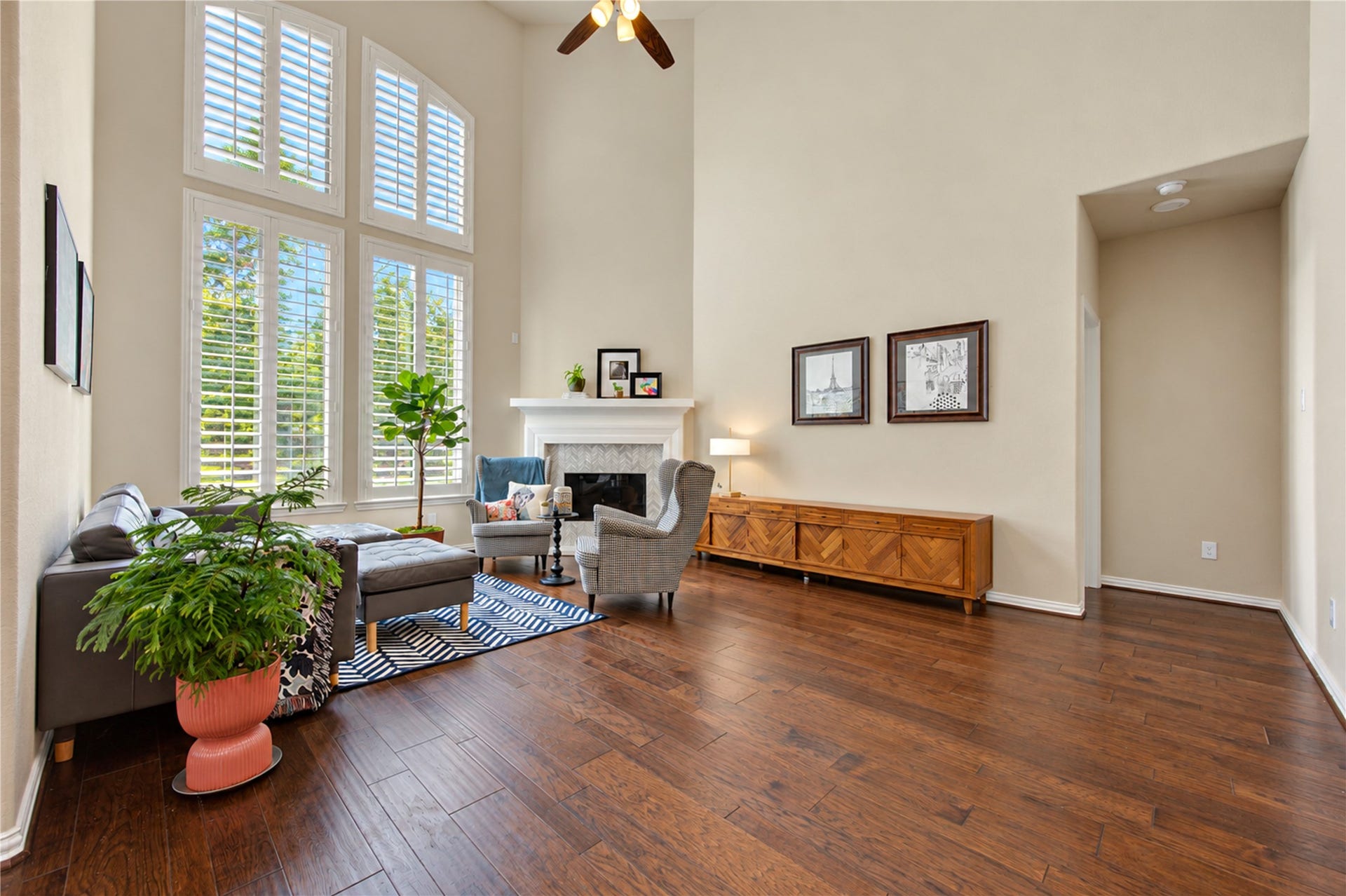 The dramatic double-height ceiling creates a grand, airy feel in the living room, complemented by a tall gas fireplace with a stylish tile surround that serves as a striking focal point.