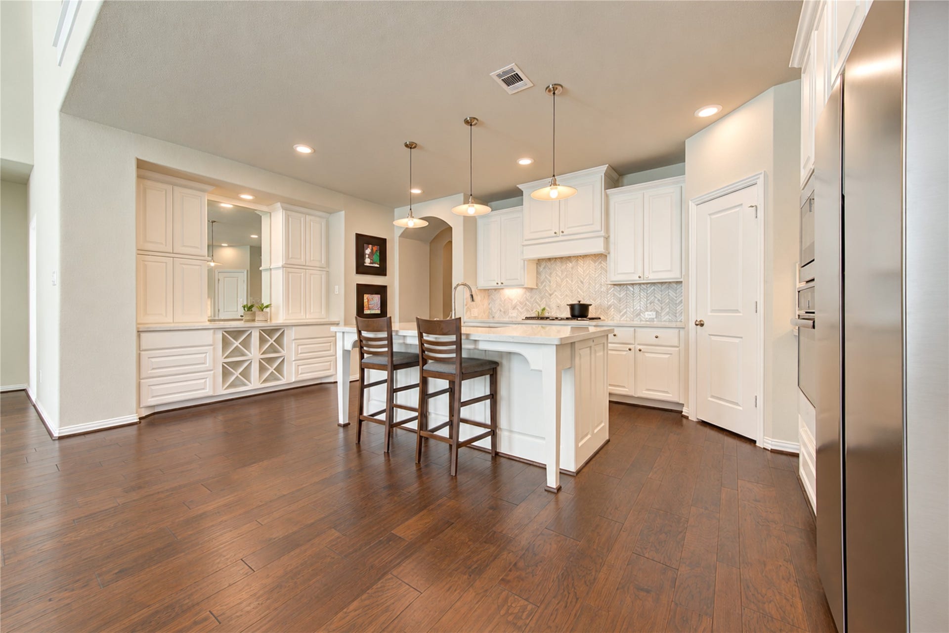 To the left of the kitchen, a convenient dry bar offers additional cabinetry and storage, while a large mirrored backsplash reflects the homes abundant natural light, enhancing the bright and open feel of the space.