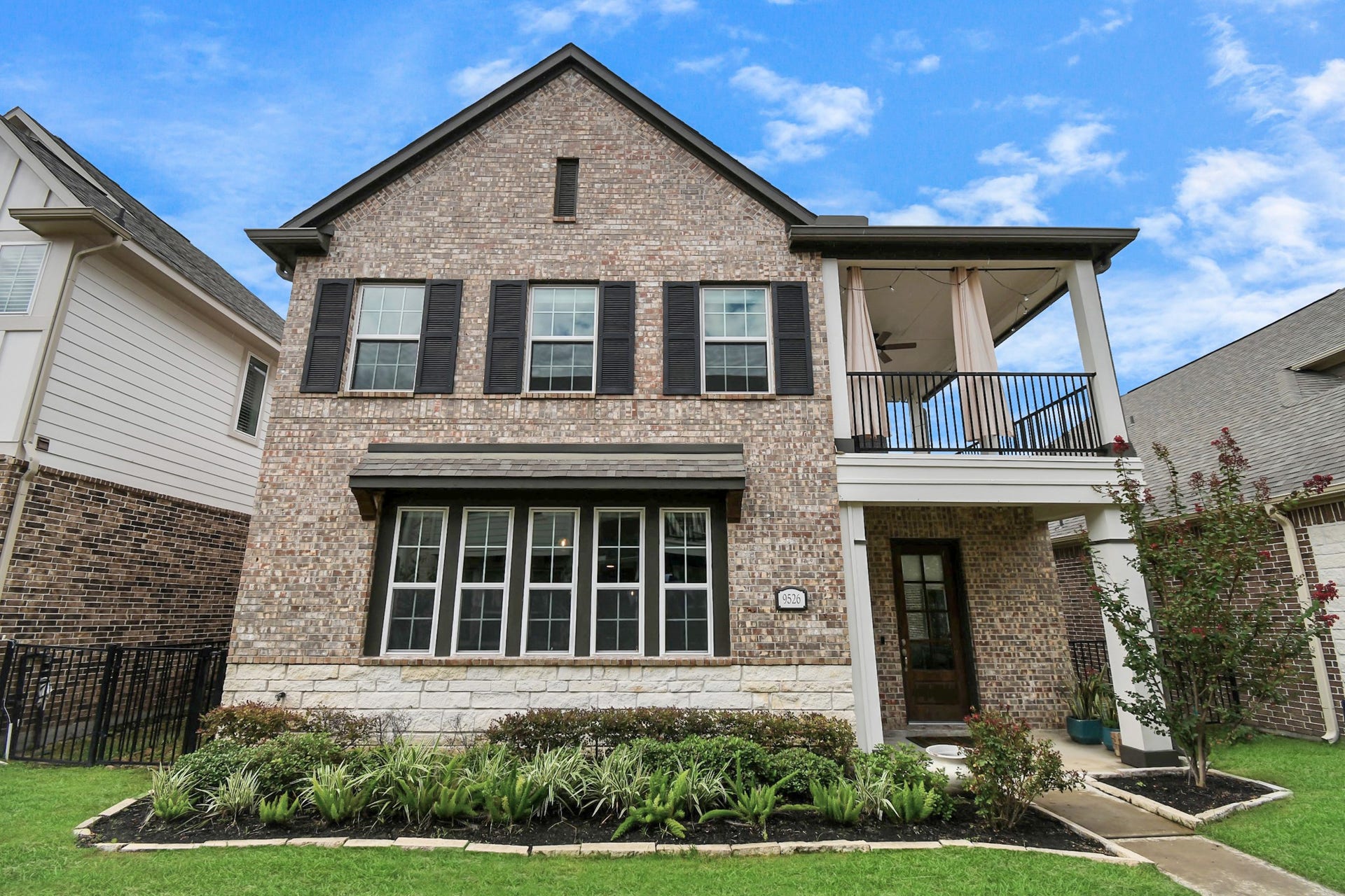 Charming two story brick home with a welcoming porch and a spacious balcony, offering great curb appeal and modern elegance.