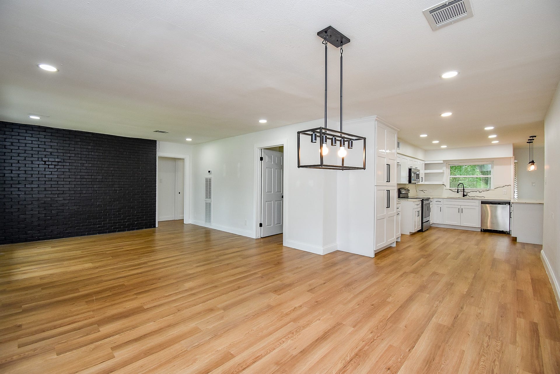 Open-concept living area with wood floors, black accent wall, and modern white kitchen.