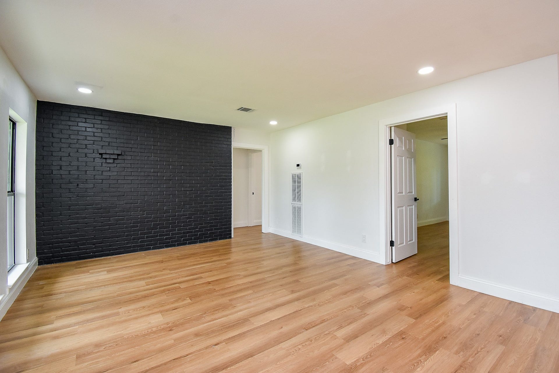 Spacious room with hardwood floors, black brick accent wall, and natural light.