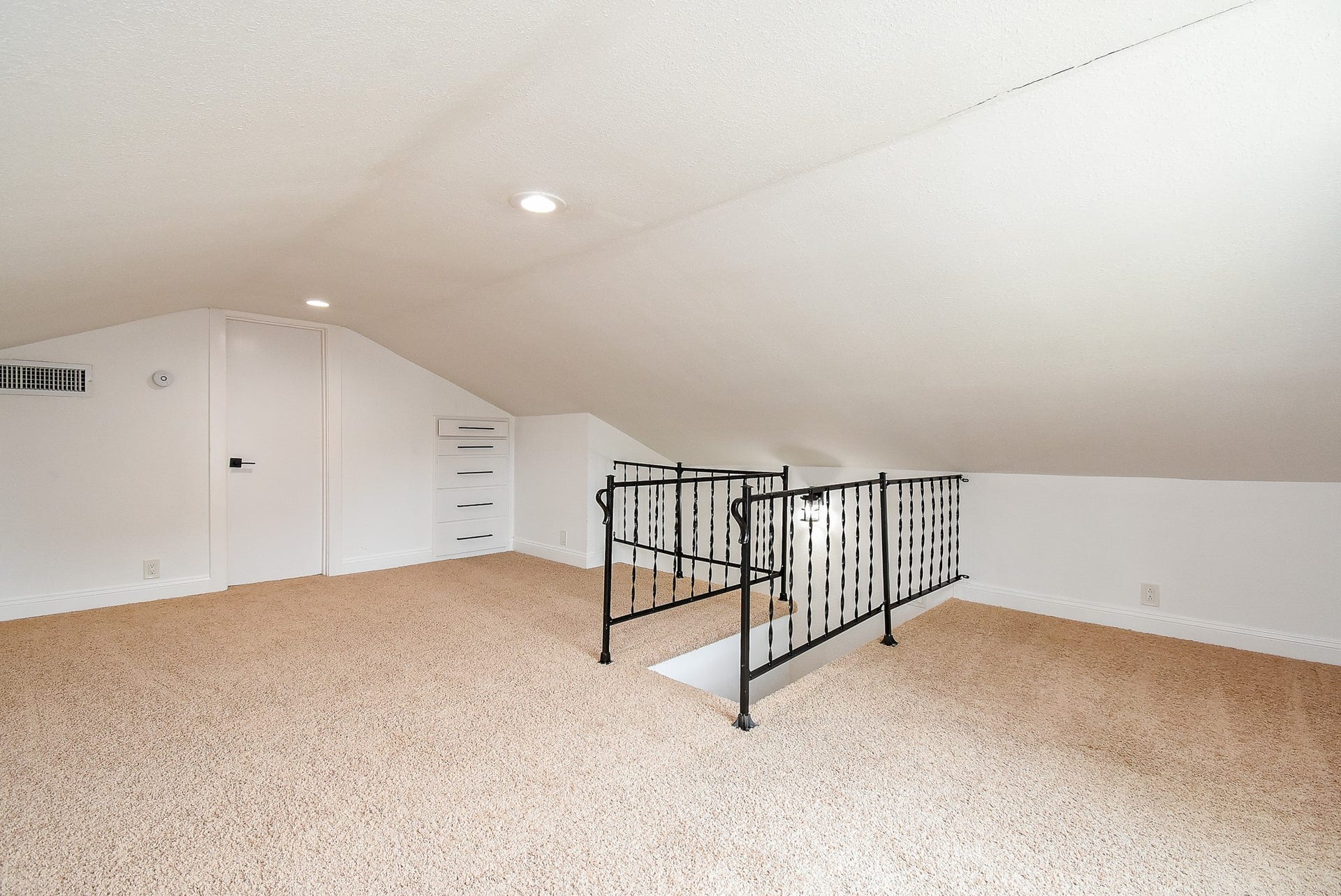 Spacious attic loft with soft carpeting, built-in drawers, and wrought iron railing.