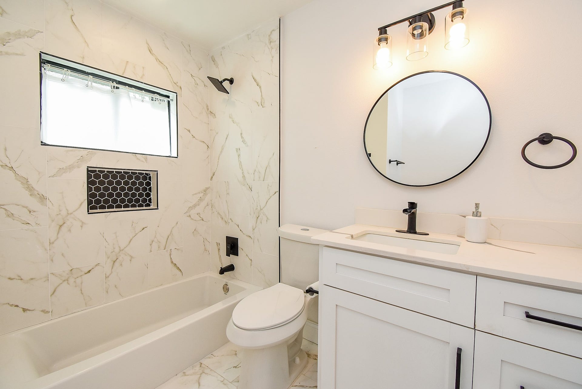 Modern bathroom with marble tile, black shower fixtures, and a white vanity.