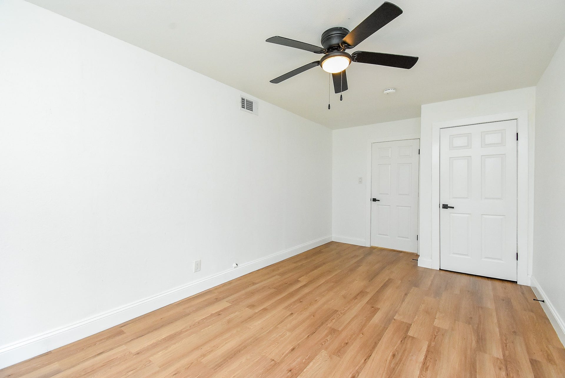Spacious room with hardwood floors, white walls, and a stylish ceiling fan.