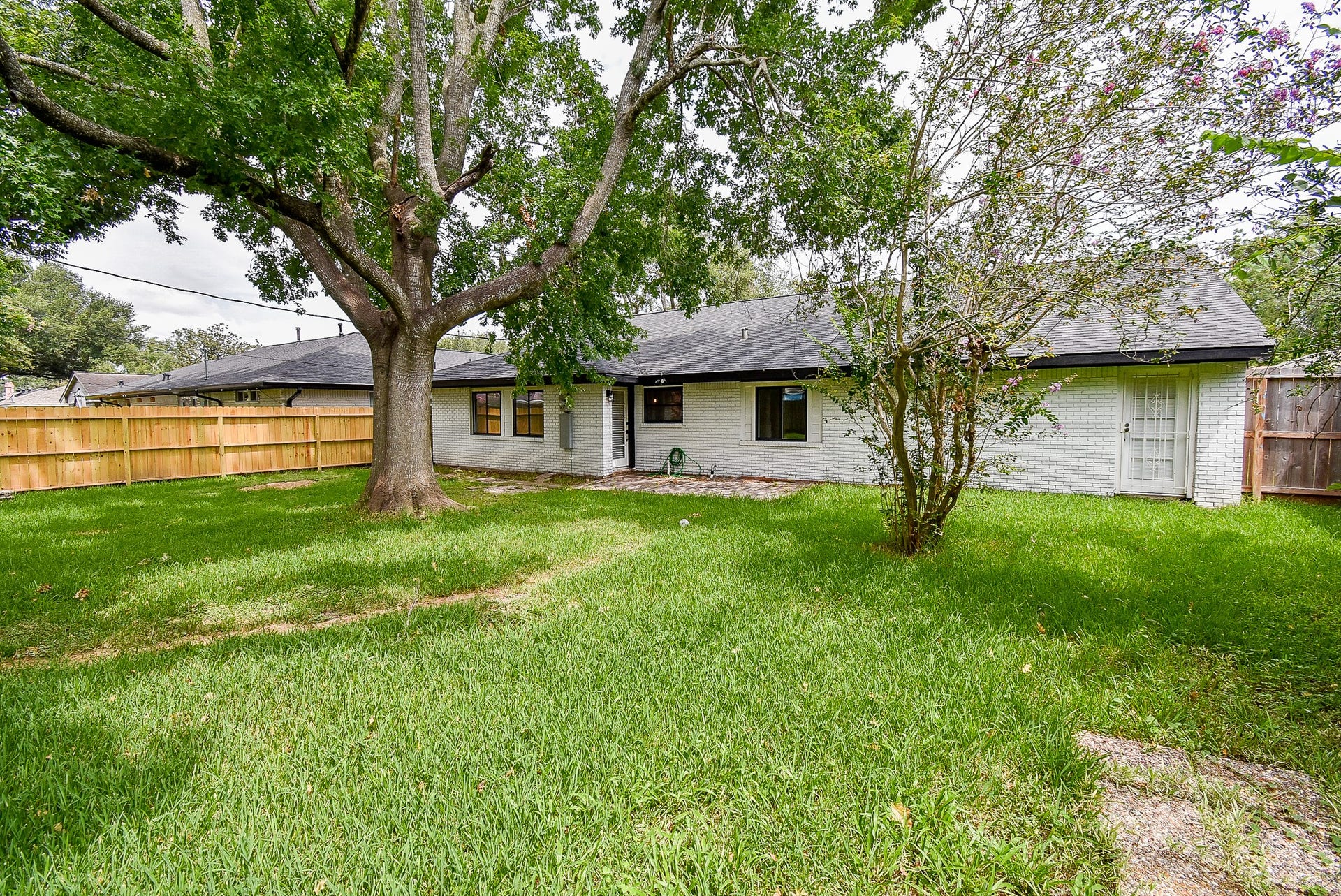 Spacious backyard with lush greenery, mature trees, and a charming brick exterior.