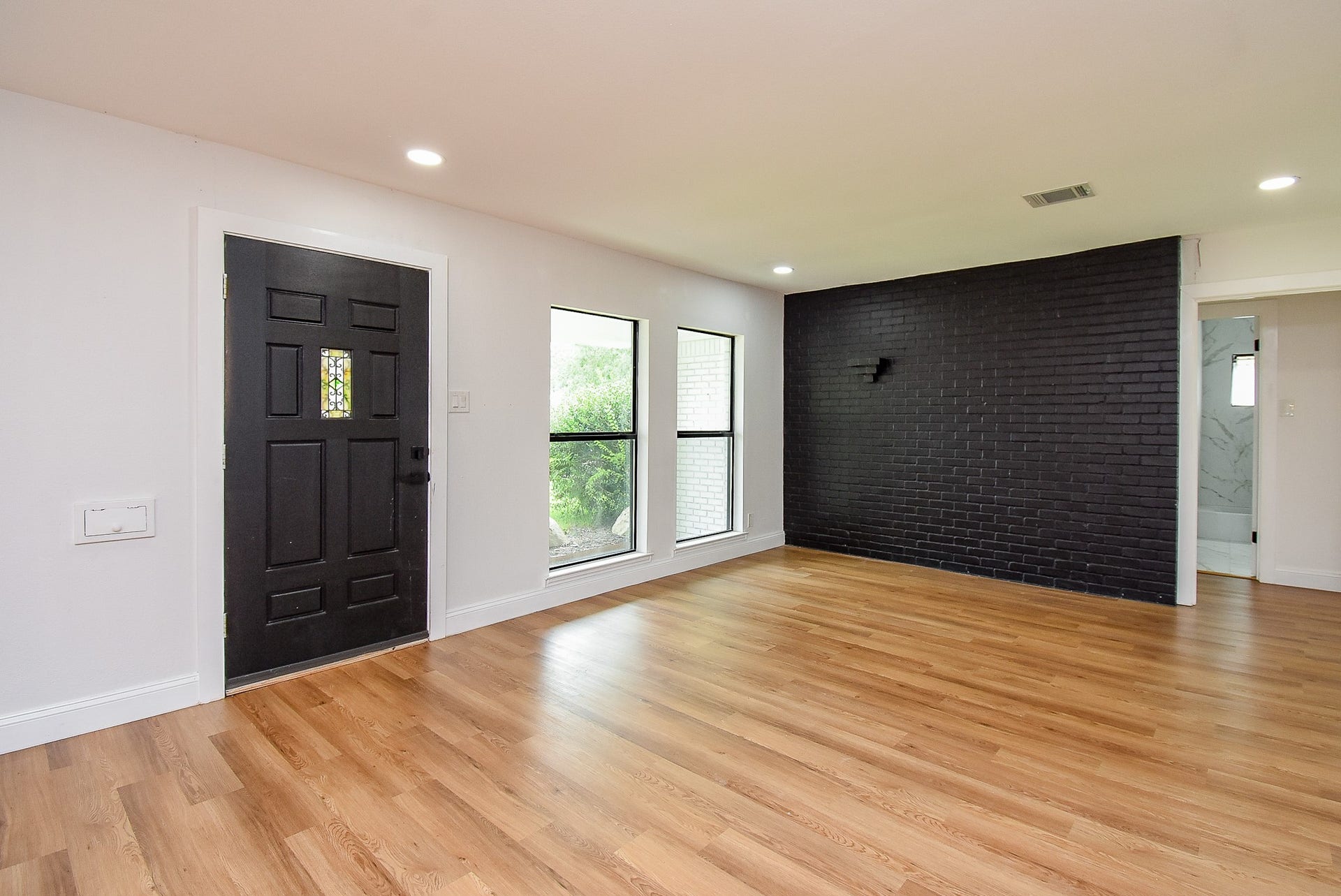 Bright living area with a black accent wall, large windows, and warm wood floors.