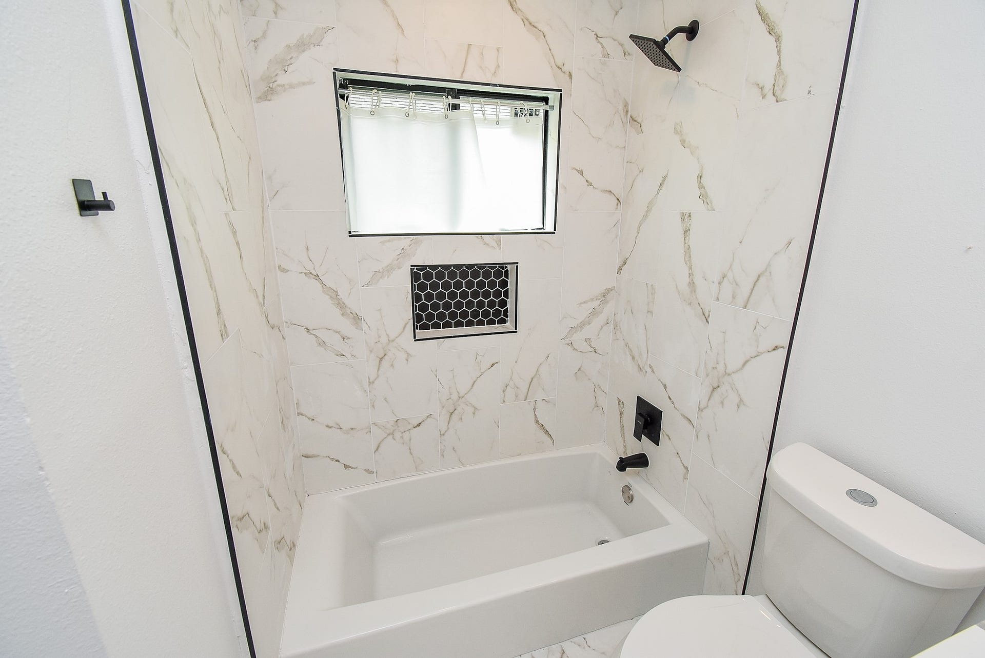 Elegant bathroom with a white tub, black fixtures, and marble-style tile.
