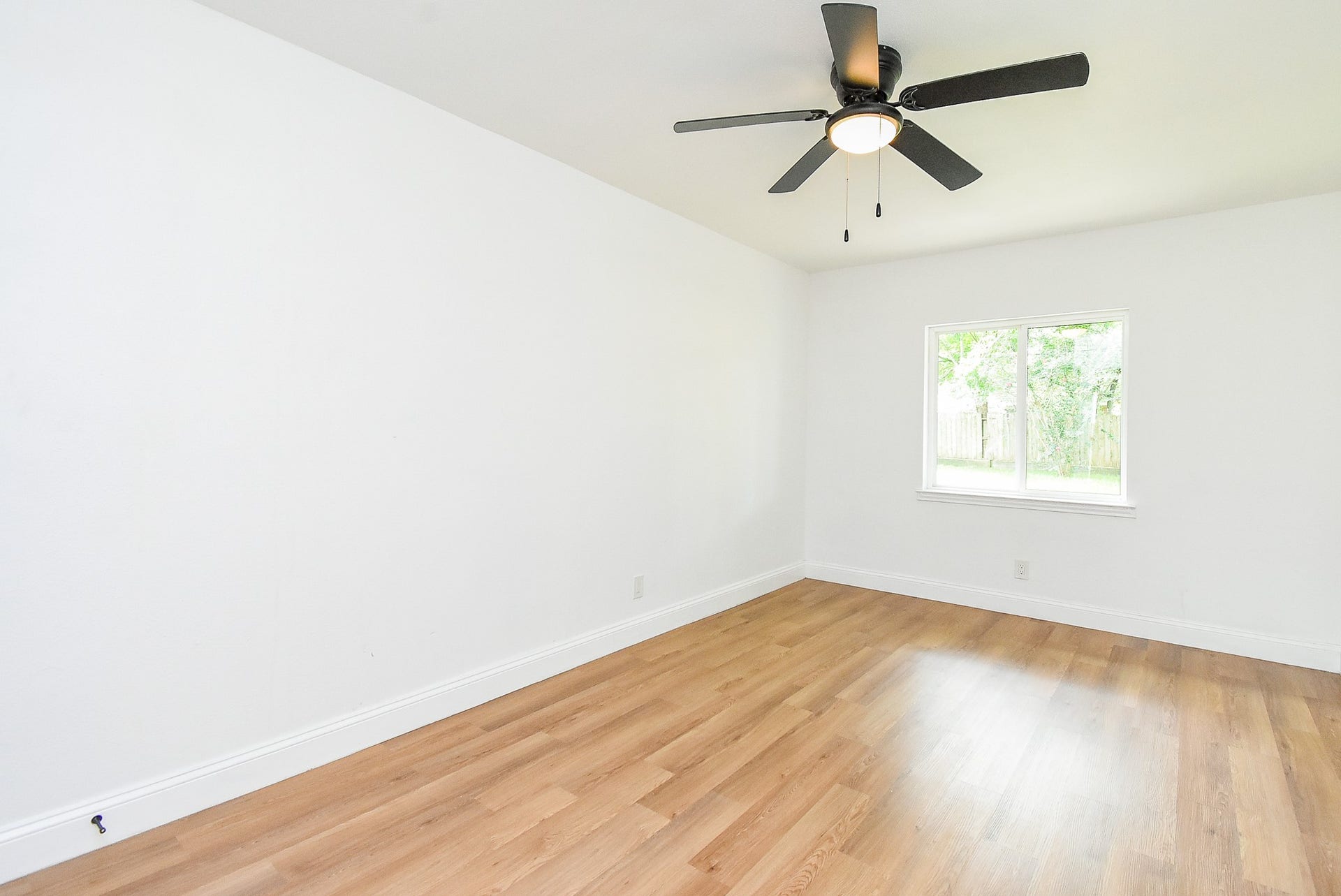 Bright room with white walls, a ceiling fan, and warm wood flooring.