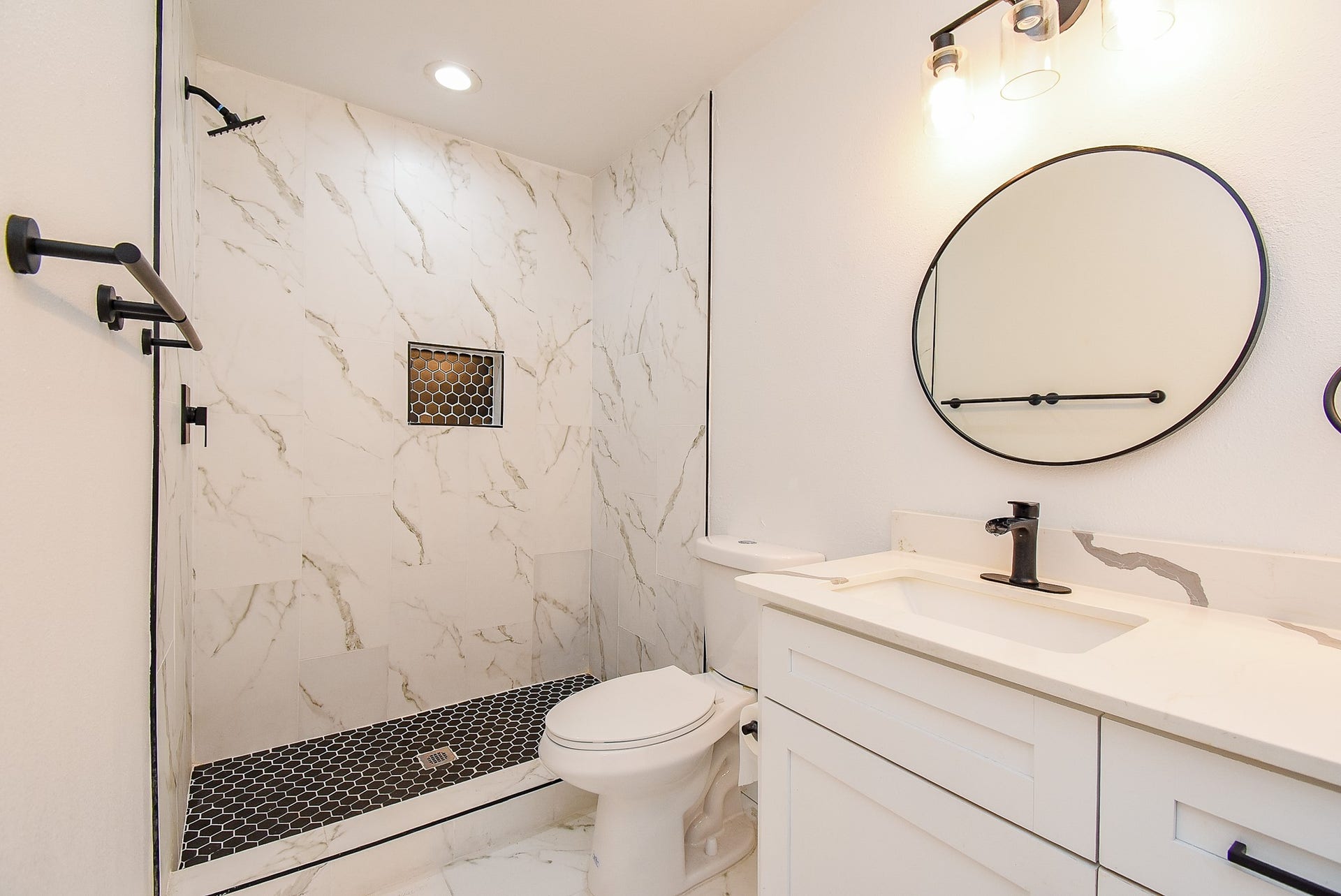 Modern bathroom with a walk-in shower, marble-style tile, black fixtures, and stylish vanity.