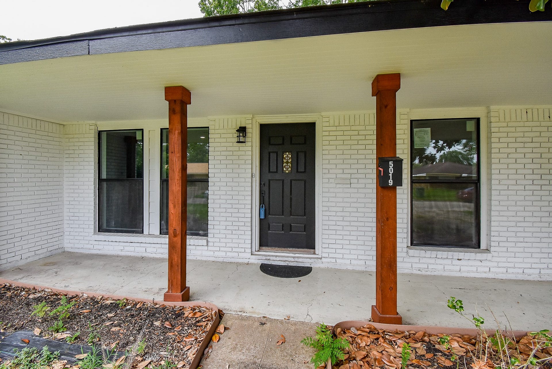 Charming front porch with wooden columns, a sleek black door, and bright white brick for an inviting entrance.