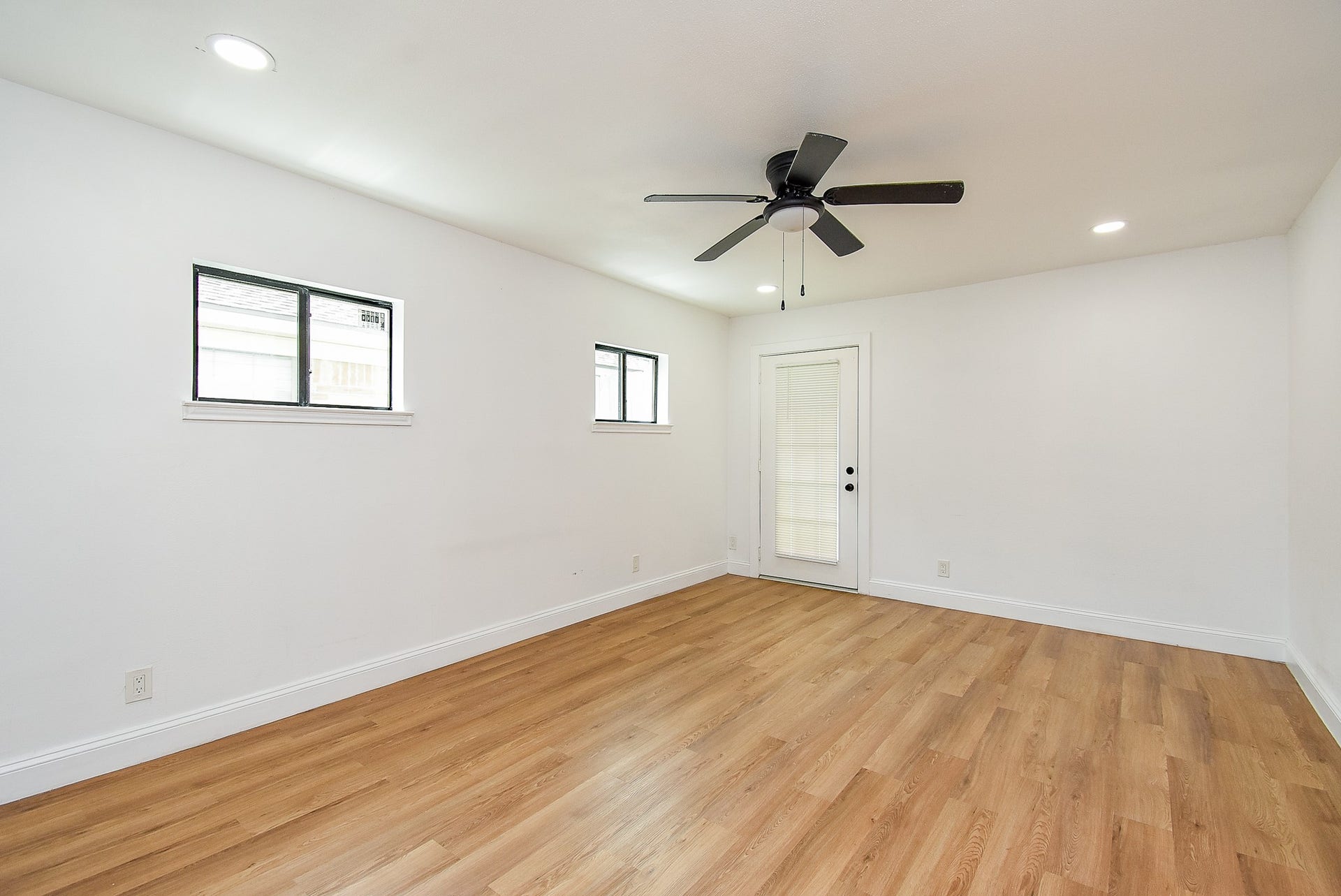 Bright room with wood flooring, a ceiling fan, and large windows for natural light.