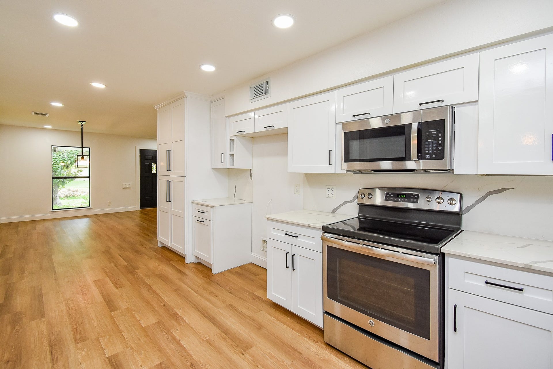 Modern kitchen with stainless steel appliances, white cabinetry, and warm hardwood floors.