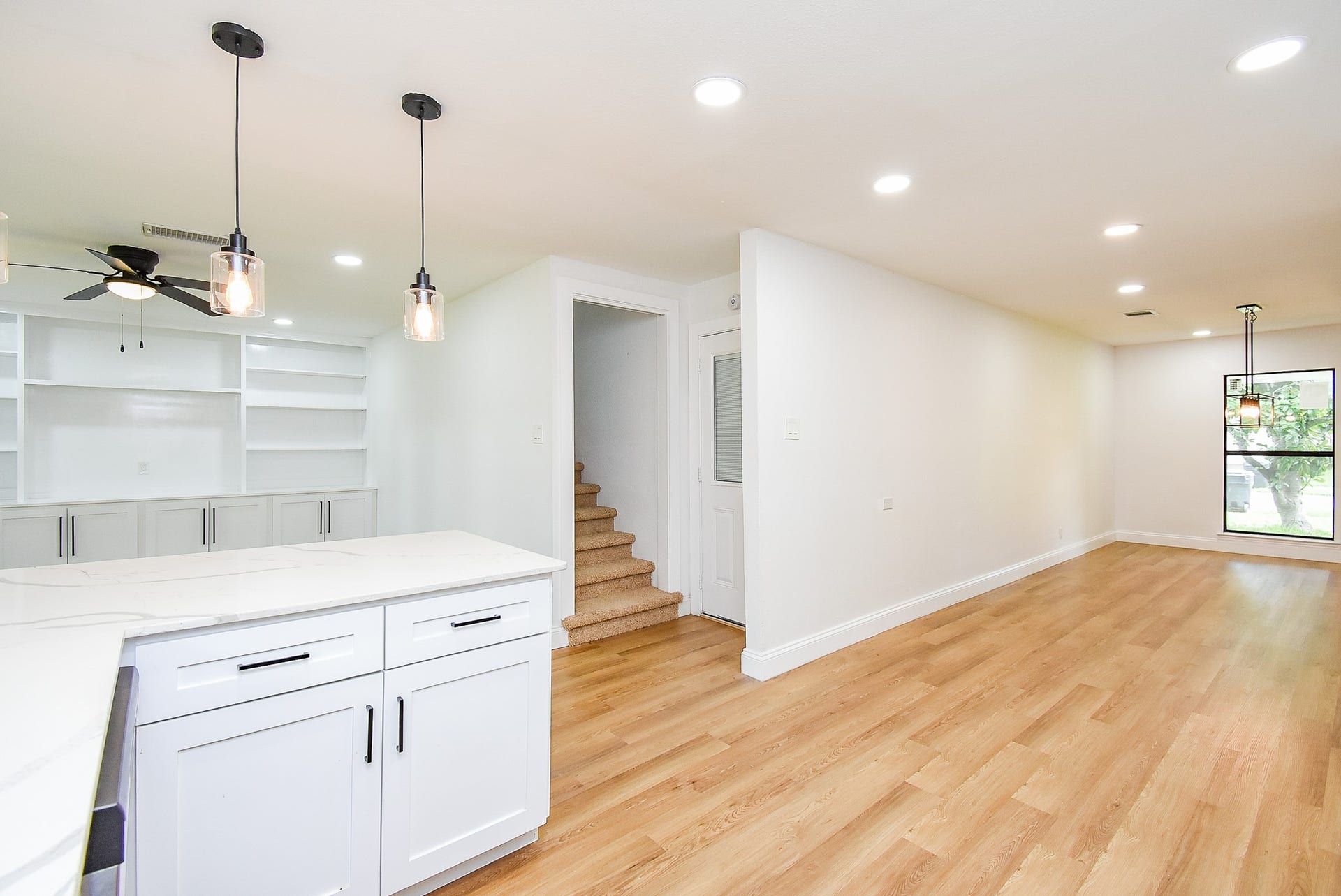 Bright open-concept space with hardwood floors, modern lighting, built-in shelving, and a stylish kitchen.