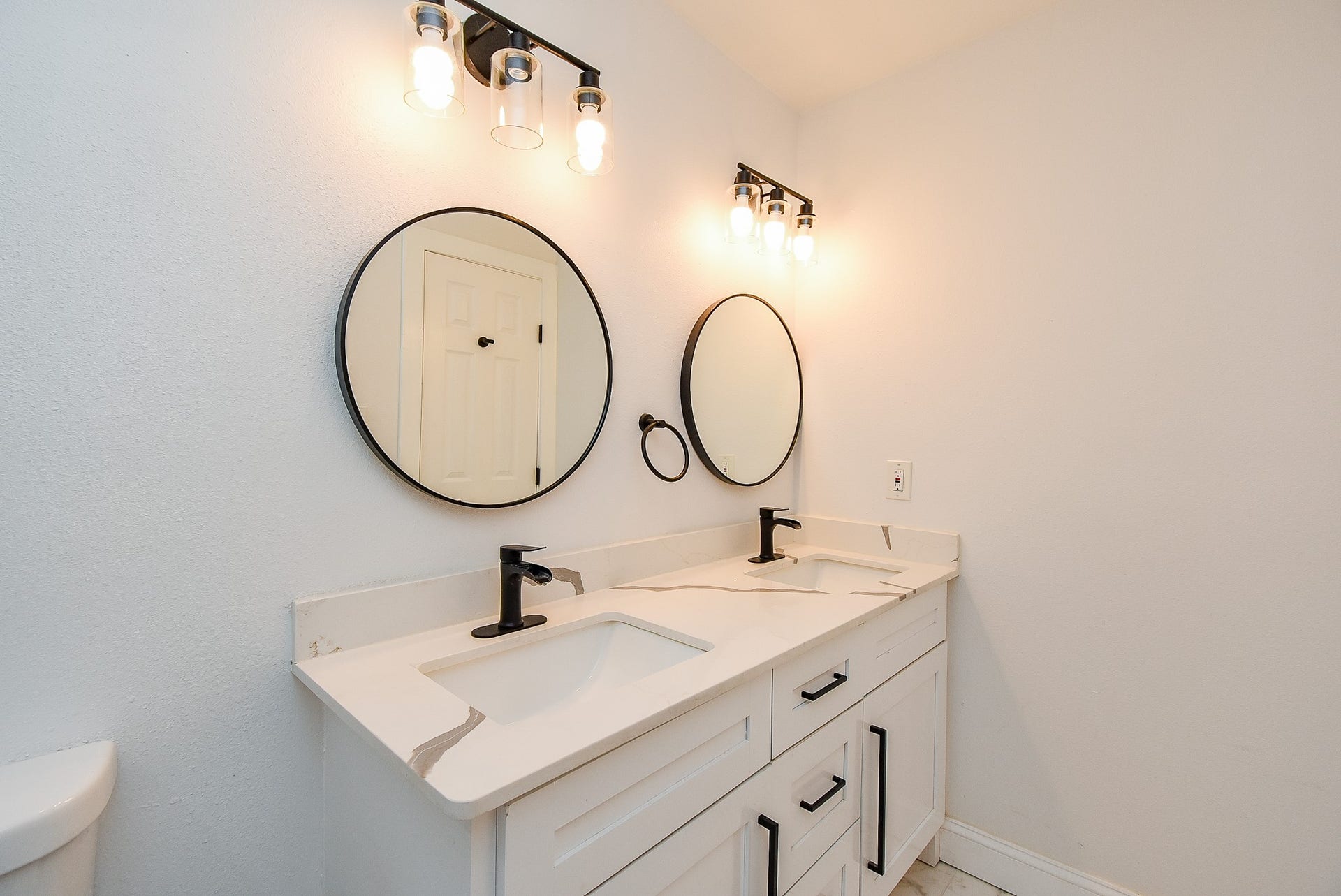 Elegant bathroom with a double vanity, black fixtures, and stylish round mirrors.