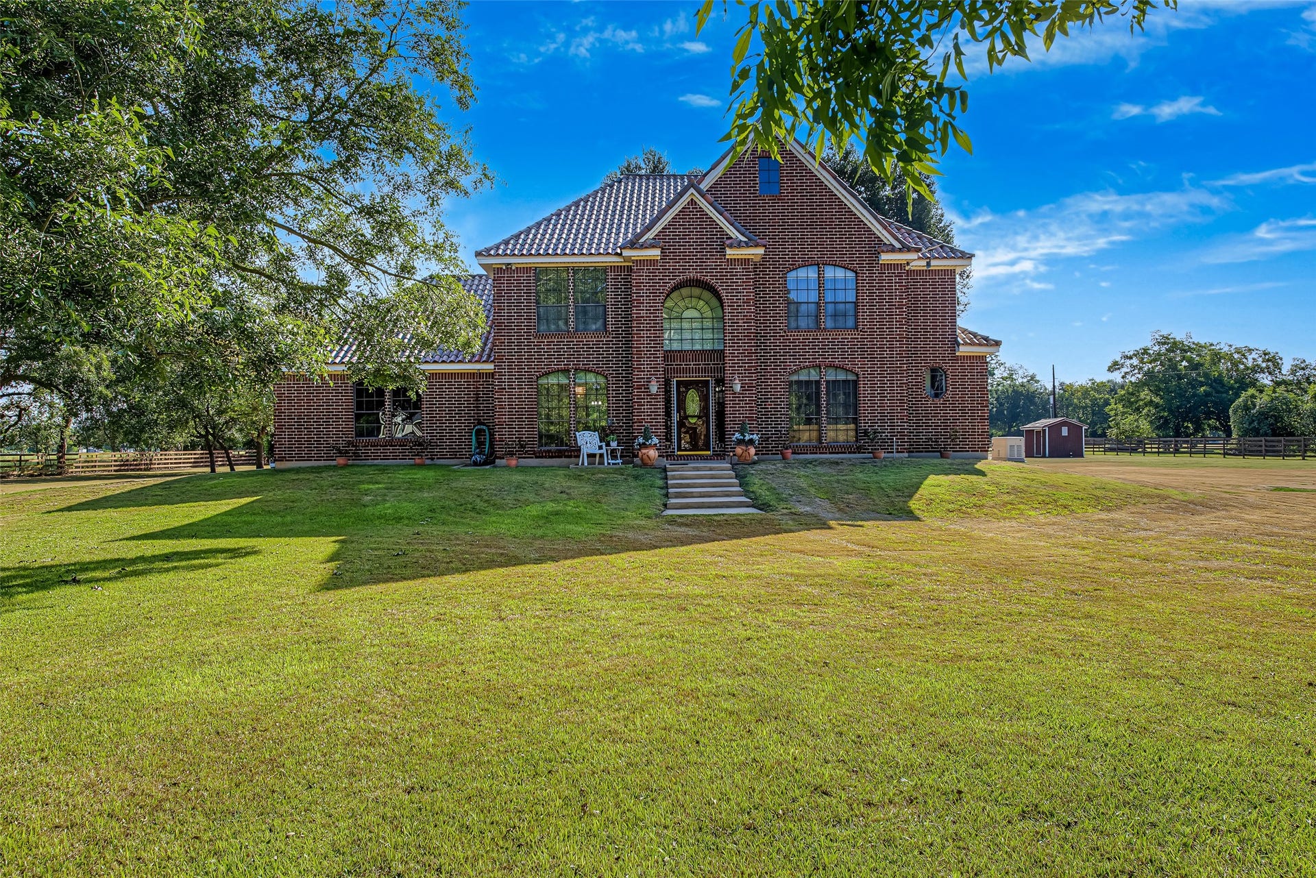 1345 Peach Ridge Road, Brookshire, TX 77423 Exuding timeless architectural elegance, the grand two-story front facade of the main residence showcases a rich, multi-tone red brick exterior complemented by a distinctive tiled roof and classic gabled rooflines.